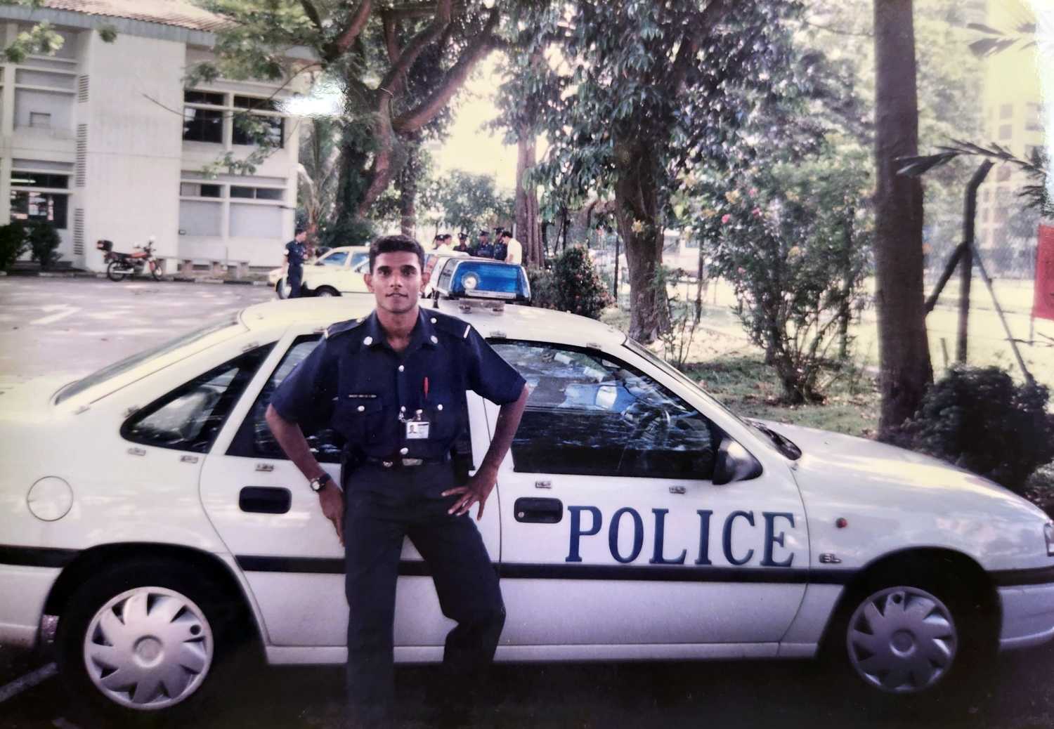 photo of a very young DSP Singh standing infront of an old Fast Response Car at a carpark.