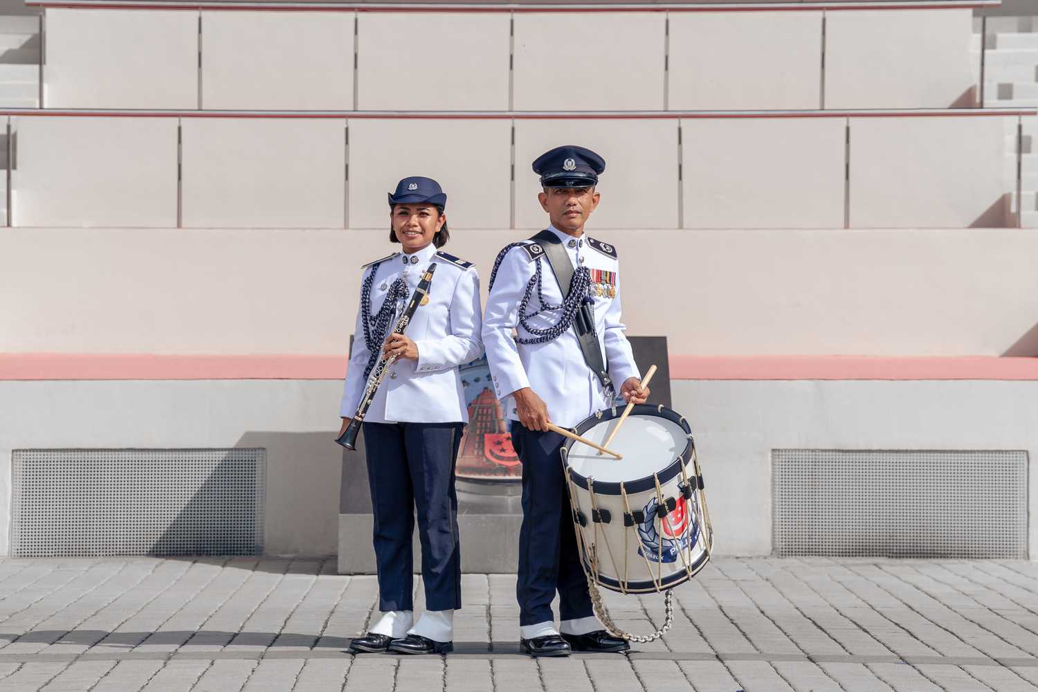 Sergeant Natassha holding a clarinet and Senior Inspector Julaimi holding an SPF drum, both standing next to each other, posing together. Both are also wearing the SPF Band's ceremonial uniform.