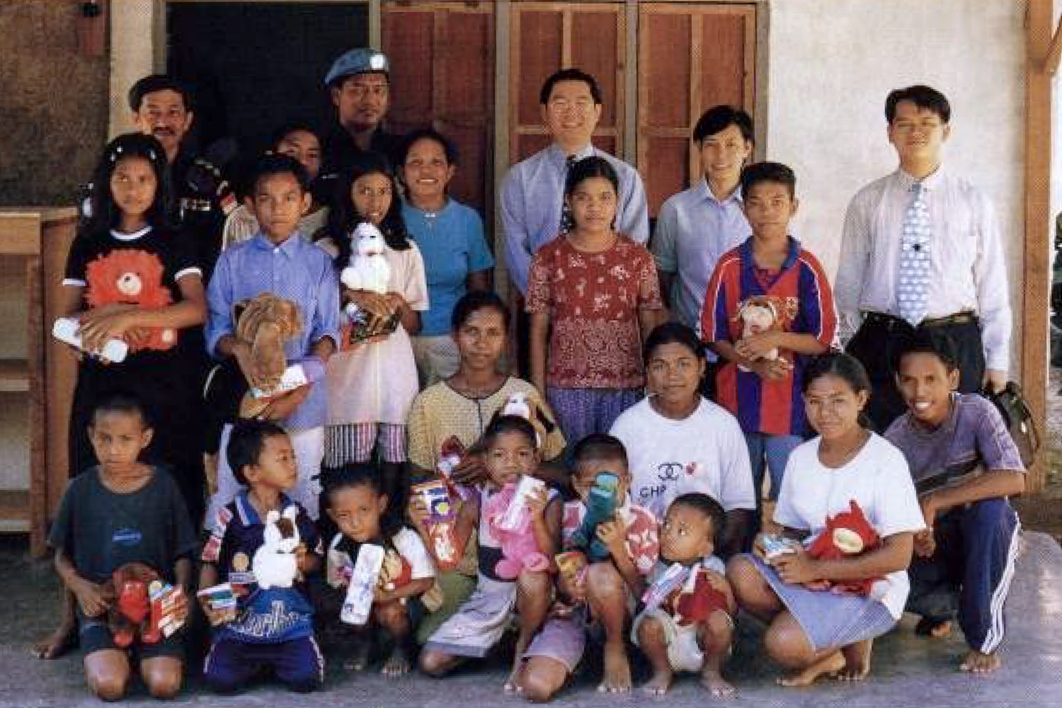 Supt Amir in uniform standing at the back, and infront of a villager's house, with many children in home clothes gathered in front.