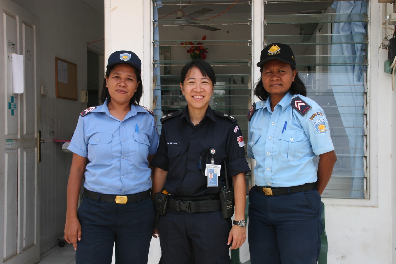 Supt Toh in the middle in uniform between two female officers from PNTL, wearing a light blue uniform and dark blue jockey cap. 