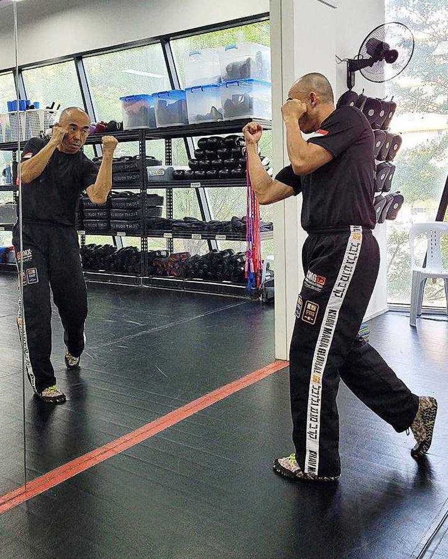 Inspector Tan Buck Song in an upper-cut pose, facing a full-body mirror in his gym. 