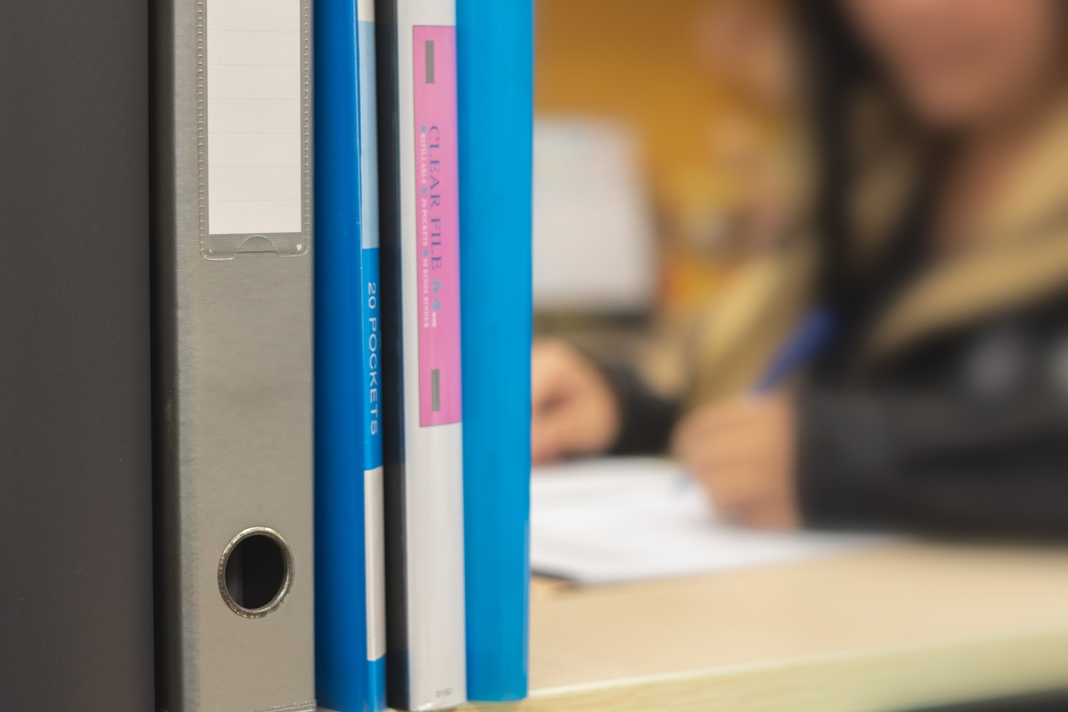 the image focuses on a bunch of files stacked horizontally with a blurred image of a female with long hair, wearing a police uniform in the background. She is writing something on paper