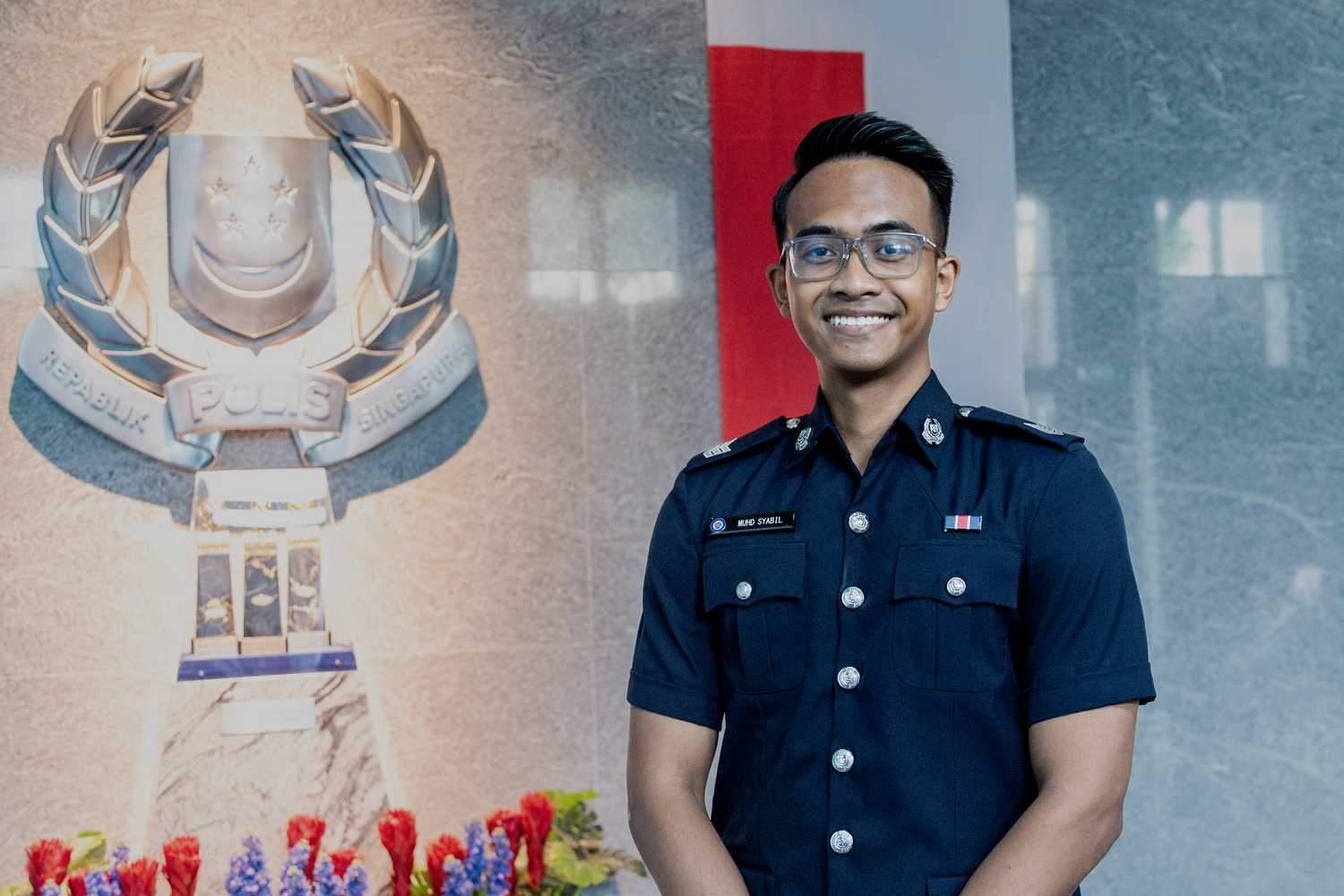 Sgt Muhamad Syabil Bin Salleh standing in front of the Singapore crest