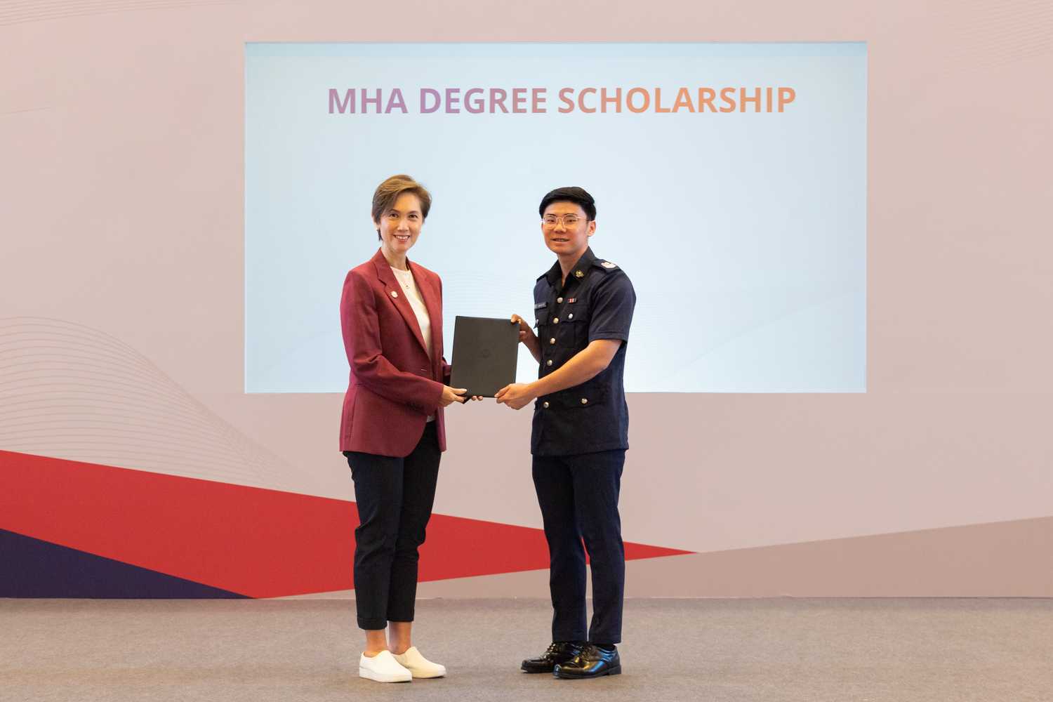 SSSgt Low receiving the MHA Degree Scholarship certificate from Mrs Josephine Teo, Minister for Communications and Information and Second Minister for Home Affairs. They are on a stage.