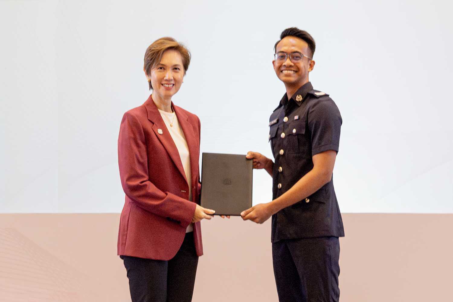 Sgt Muhamad receiving the MHA Degree Scholarship certificate from Mrs Josephine Teo, Minister for Communications and Information and Second Minister for Home Affairs. They are on a stage.