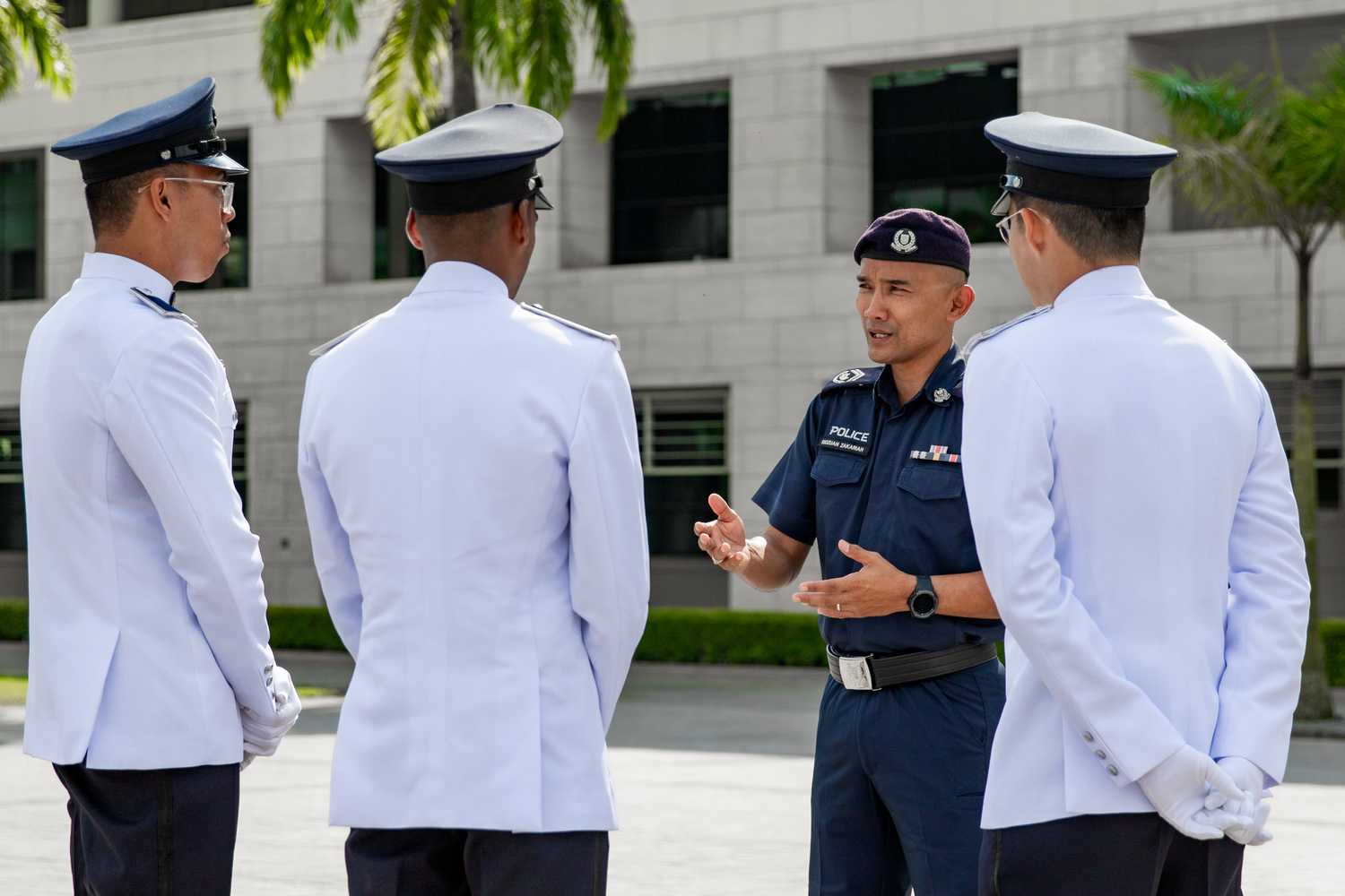 photo of the three officers in white ceremonial attire, with their backs faced, looking at SI ridzuan, who is giving instructions and talking to them