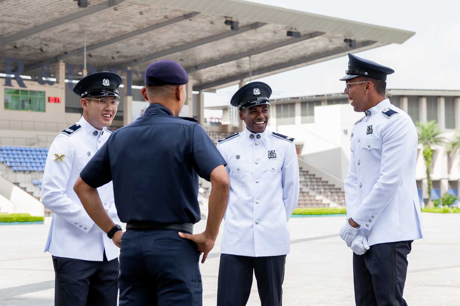 back of SI Ridzuan in the foreground with three officers in white ceremonial attire and dark blue pants, in the background facing photographer. They are smiling and laughing while talking