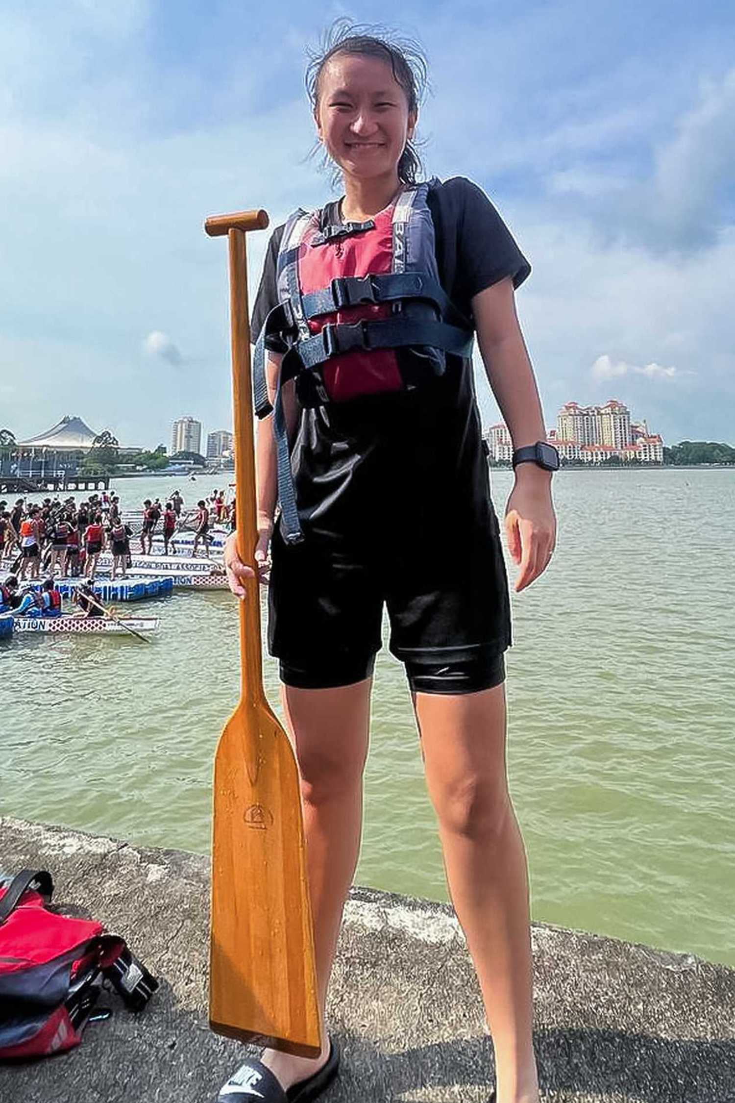 Sergeant Ivie standing with her dragon boat paddle, posing for the camera with a wide smile. 