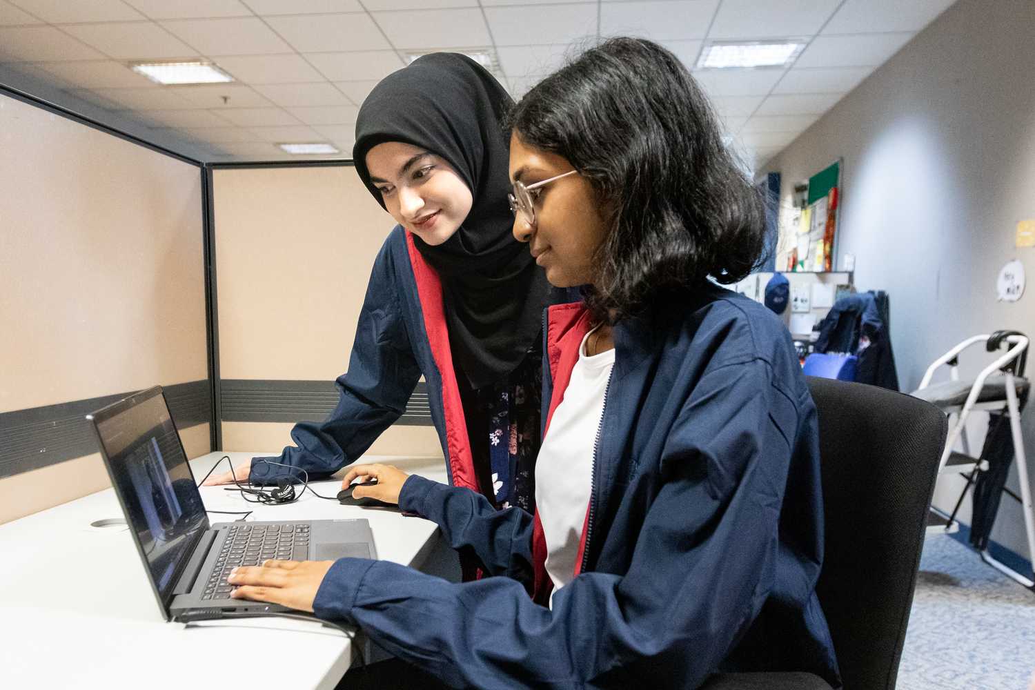 ashwini and ihshana in an office cubicle working on a laptop