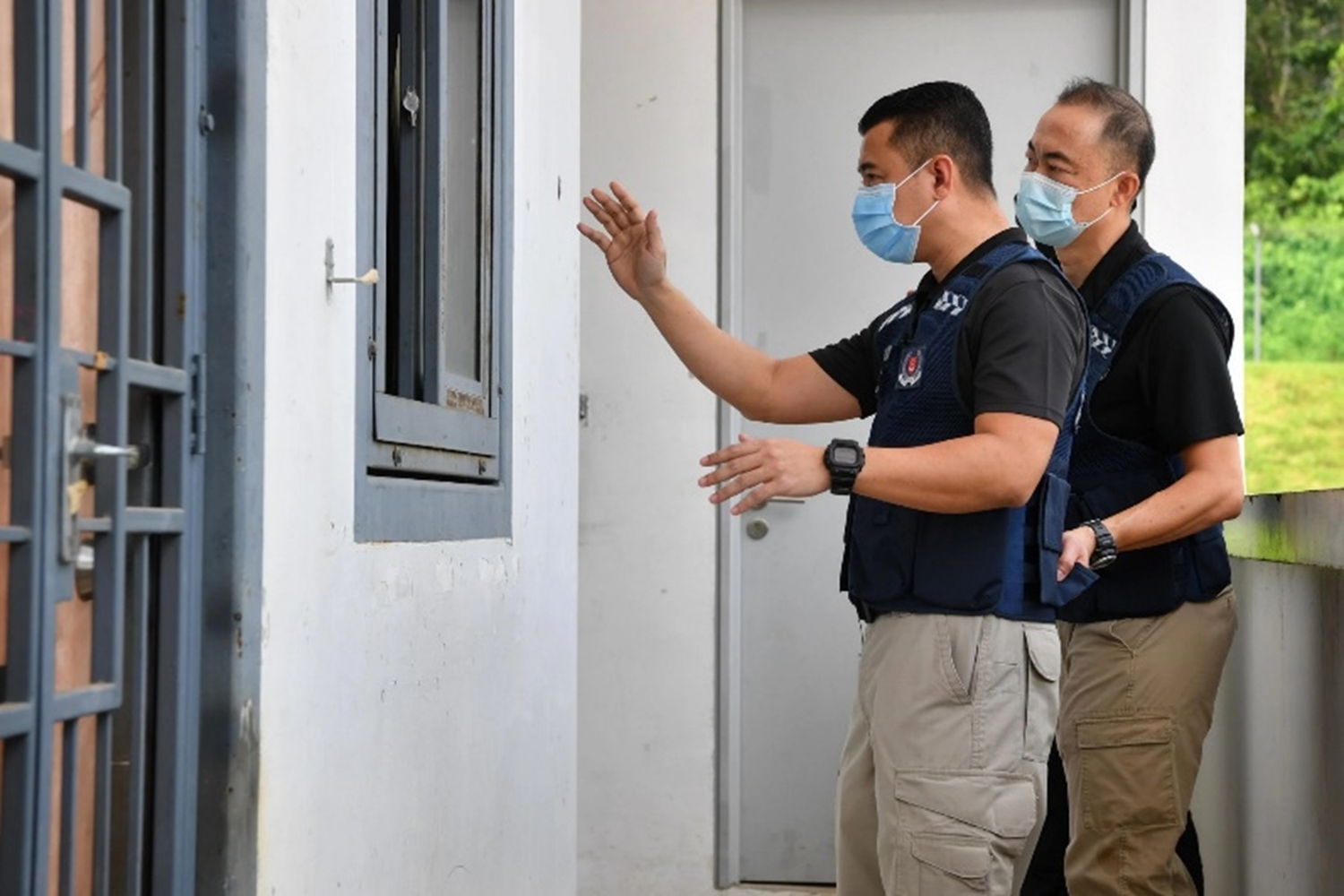 two officers facing a hdb unit and talking to someone behind a locked gate.