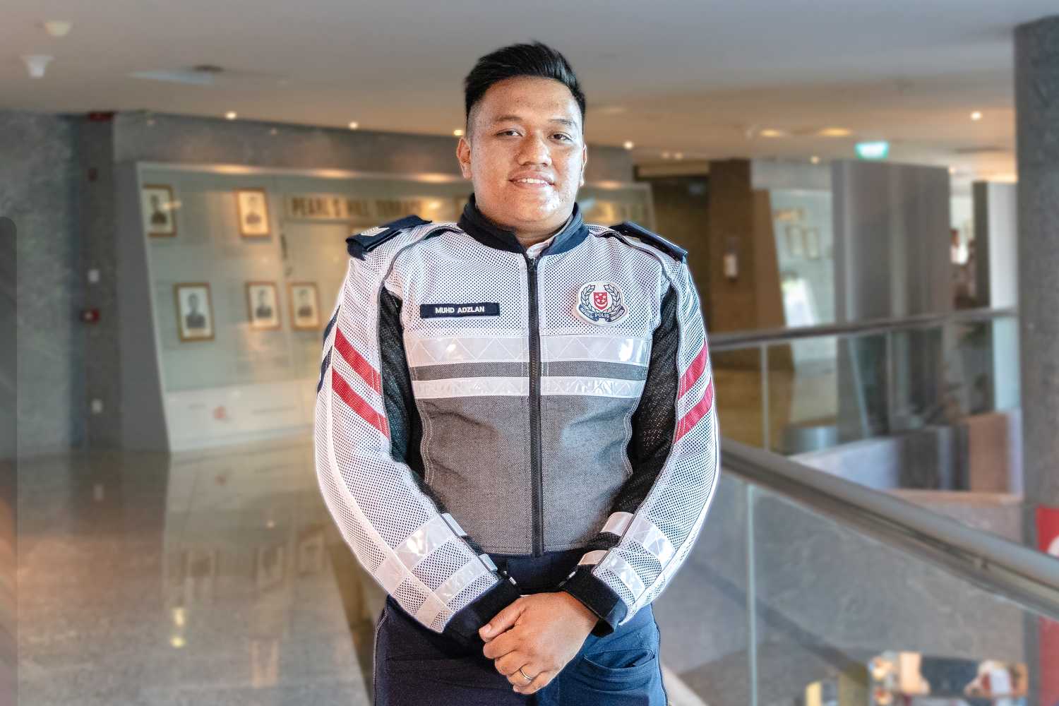 Sgt Adzlan with his hands folded in front of him, looking proudly at the camera and smiling in uniform