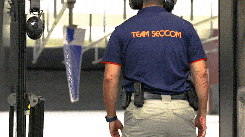 officer wearing a blue coloured polo tee with the word "seccom" in the back, shooting a gun