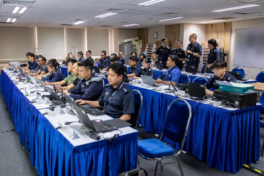 Two rows of Singapore Police Force officers, in uniform, and seated within the operations room on the day of the disposal, ready for the disposal exercise to begin. They are looking at their computers.