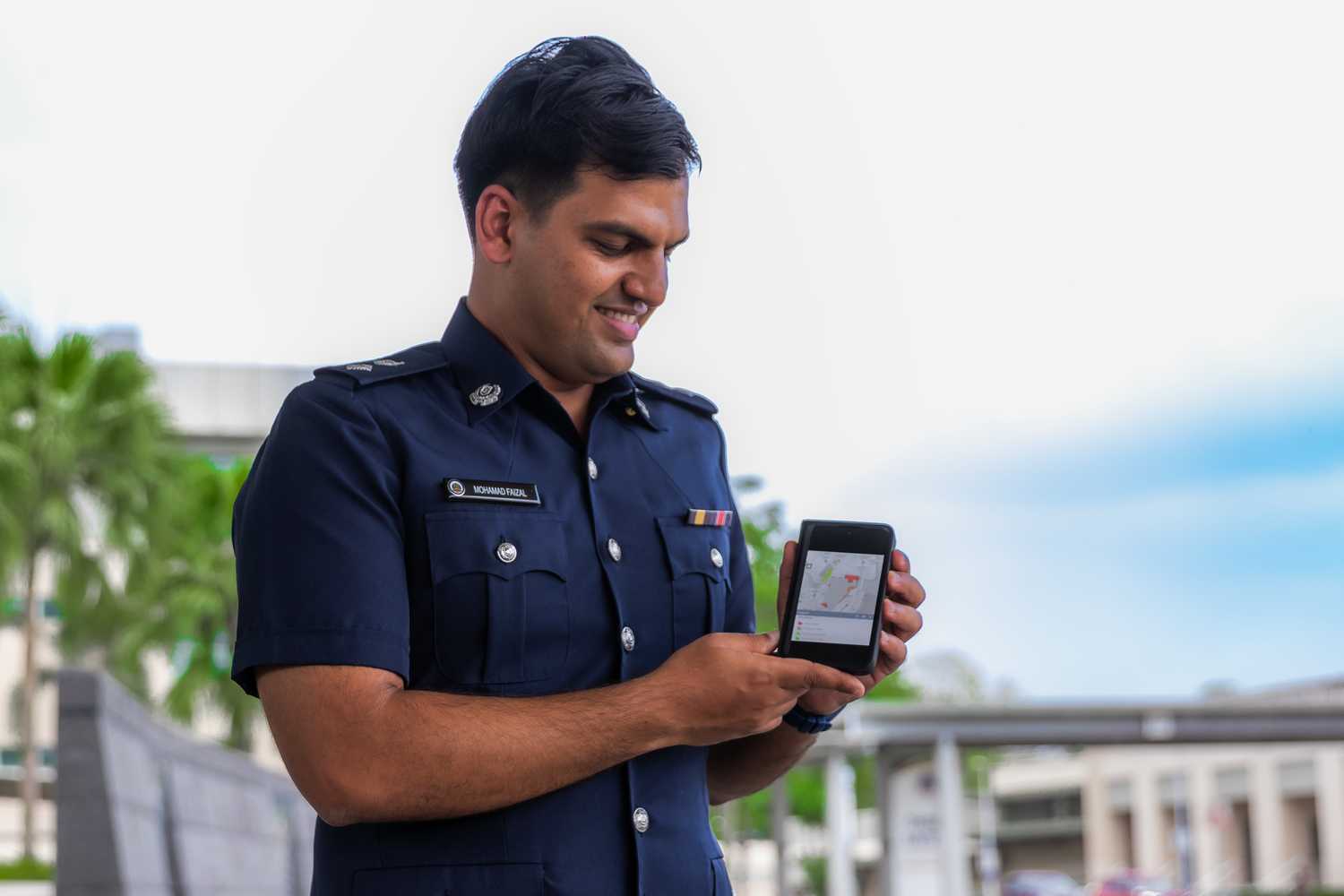 DSP Mohamad Faizal holds up a phone to the camera, where the Crowd@MarinaBay online map is shown on his phone screen. He is looking down at the phone, smiling, and looking proud.