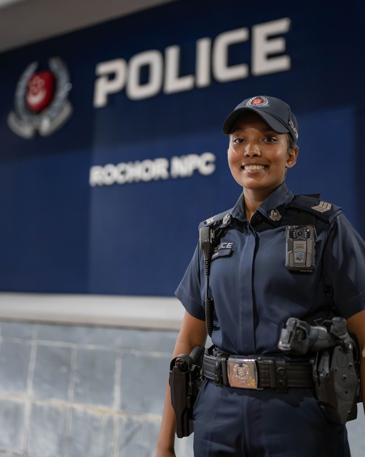 indian female police officer standing infront of police signage that says rochor npc