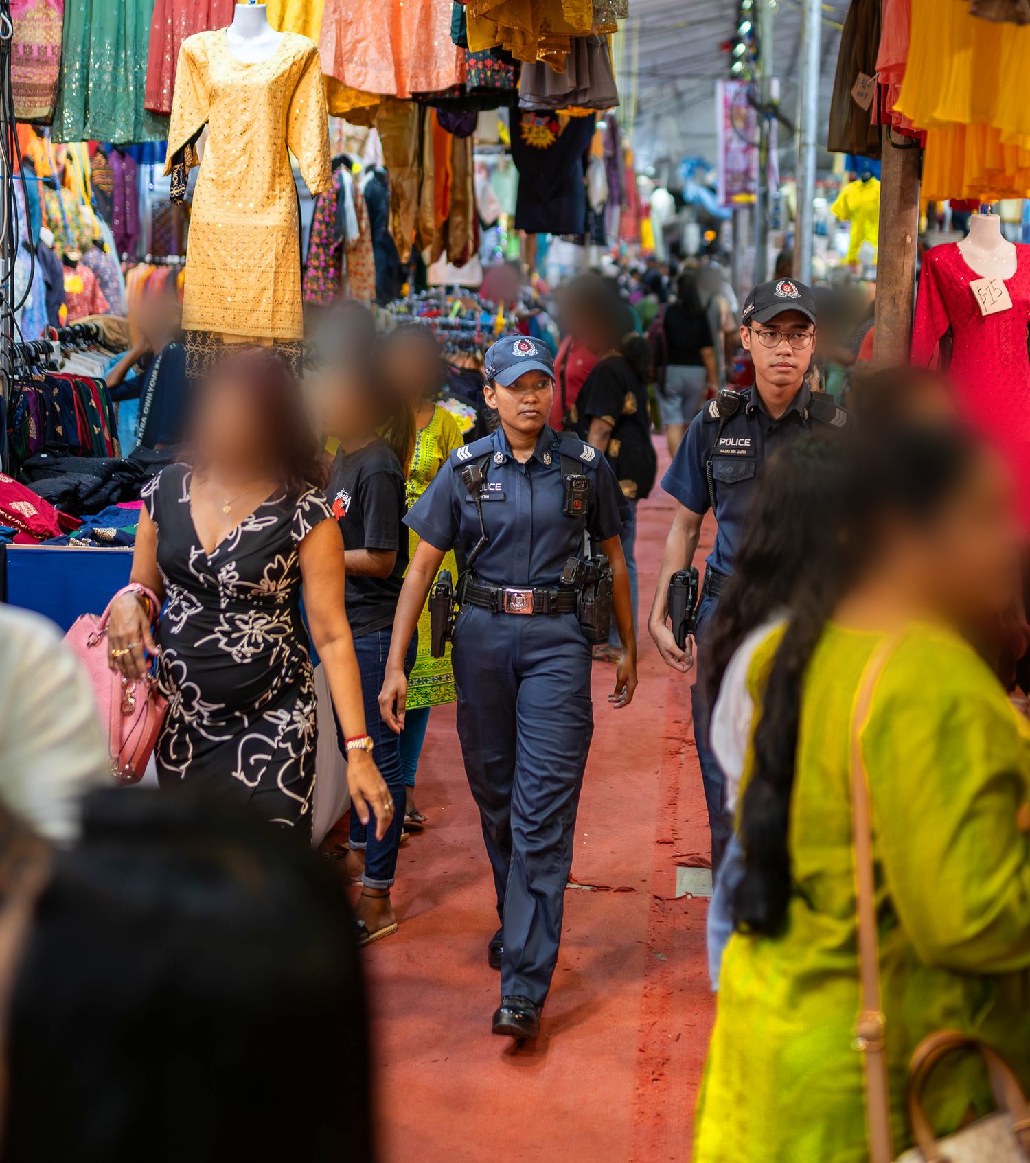 officer walking through the deepavali bazaar amidst many people wearing traditional indian clothes and colourful deco hanging