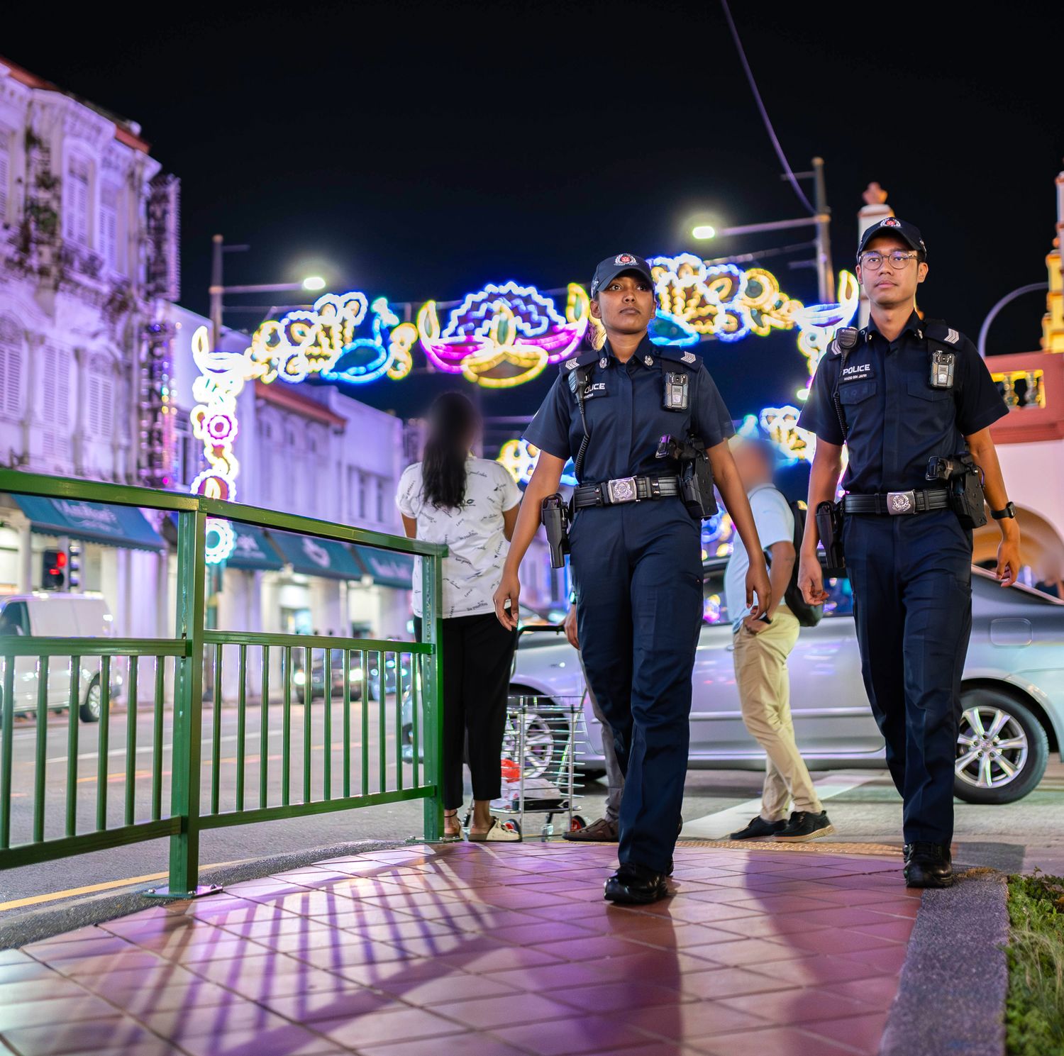 officer walking on the sidewalk with her partner, with the deepavali street light deco in the background