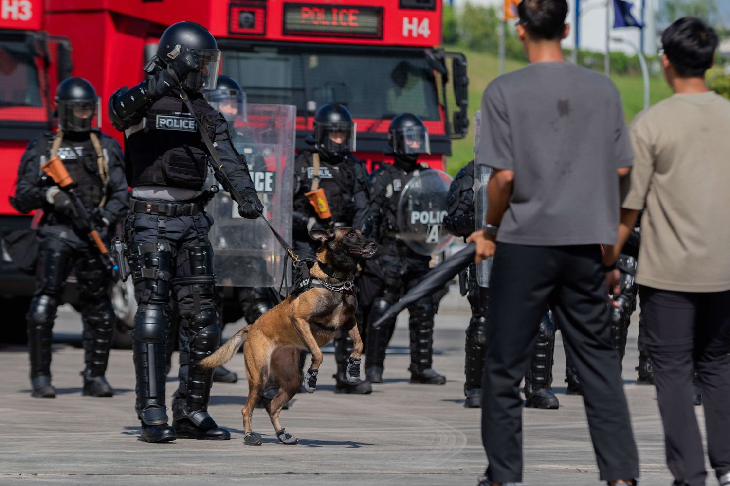 SOC officer stands infront of a mob, holding onto the leash of a german shepherd which is barking at the mob
