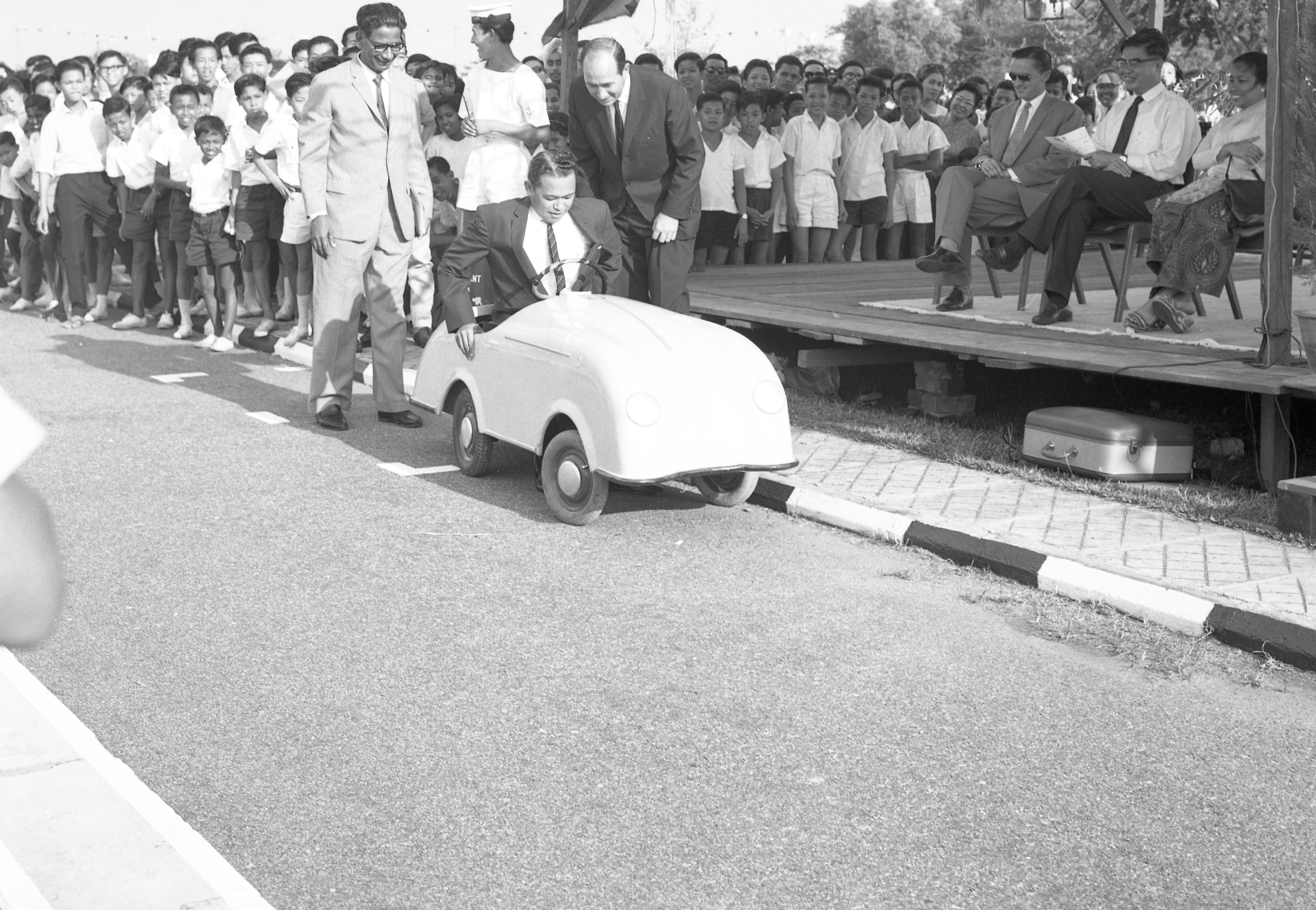 A historical black and white photograph.The photo depicts Mr Othman Wok, then Minister for Social Affairs, opening the Shell Traffic Games at the Road Safety Park at Kallang on 6 March 1964. He is sitting in a go-kart.