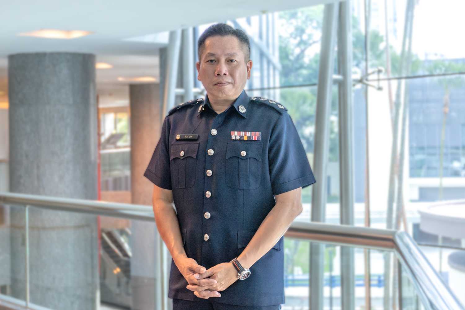 Superintendent of Police (Supt) Roy Lim is standing proudly looking at the camera in a profile shot, with his hands neatly placed in front of him.