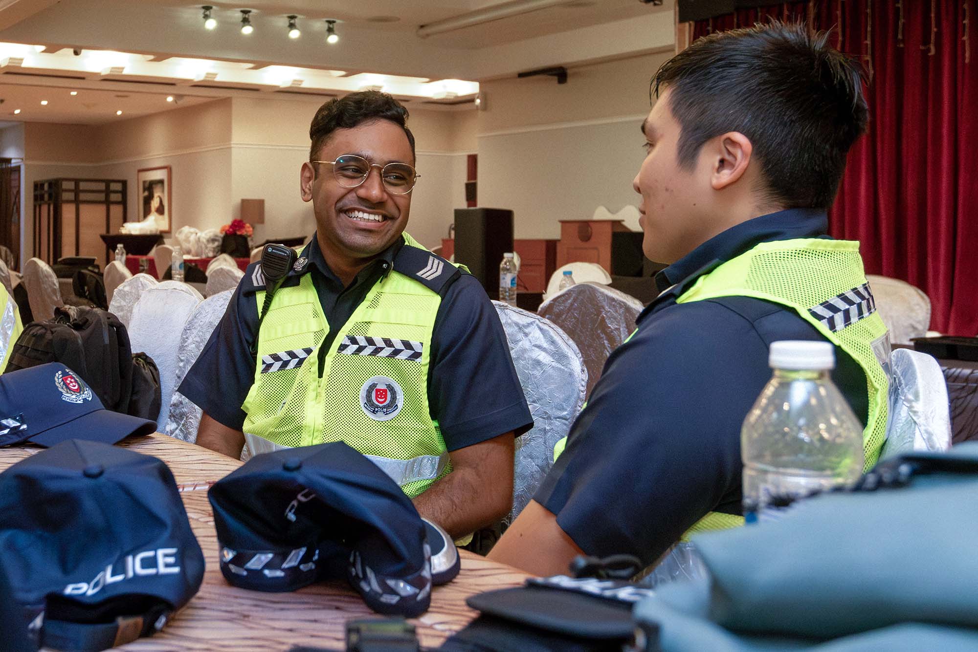 two officers seated in a room talking. Both are wearing uniform but a green vest over their attire