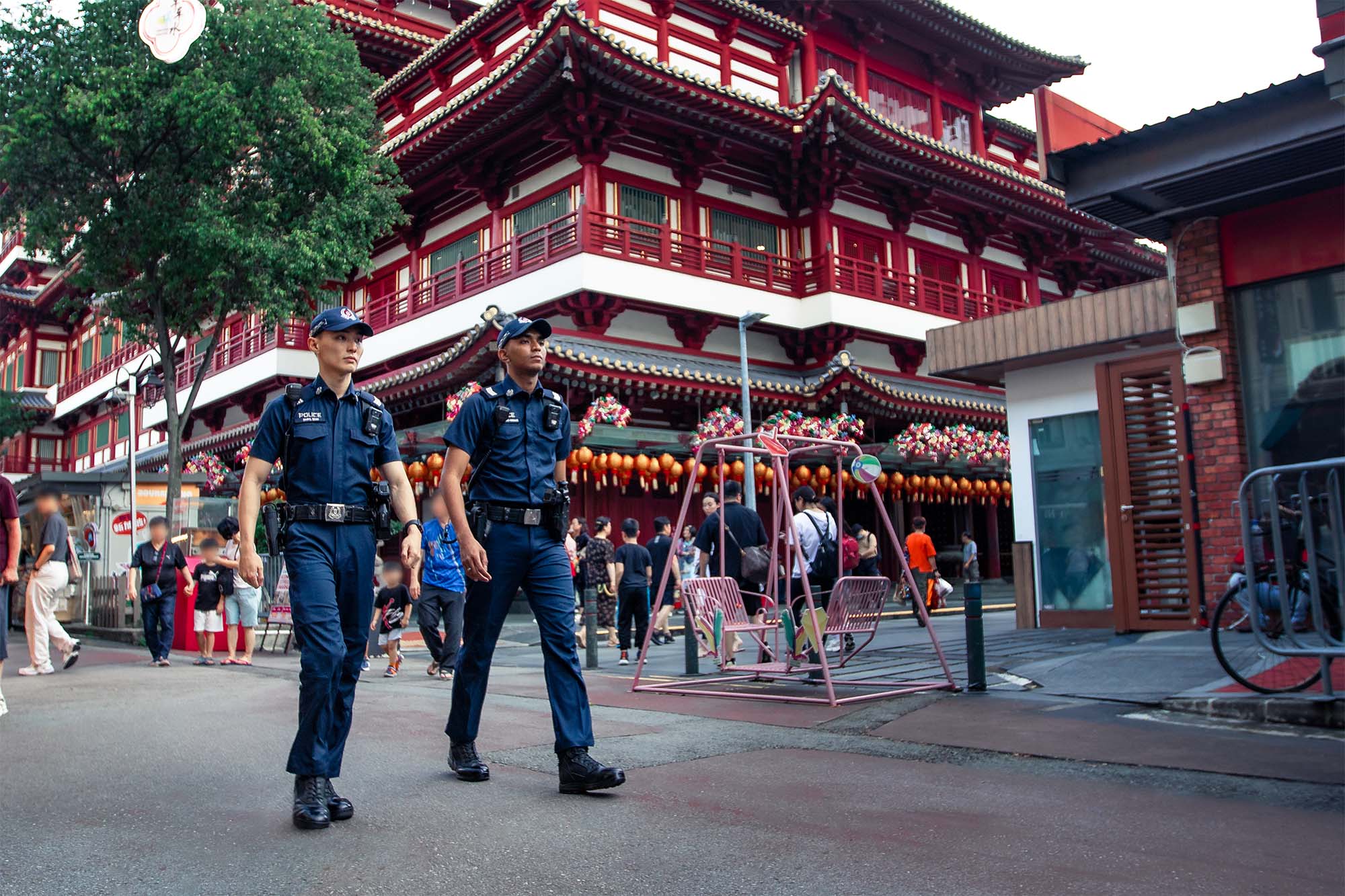 two male police officers walking. behind them is the buddha tooth relic temple