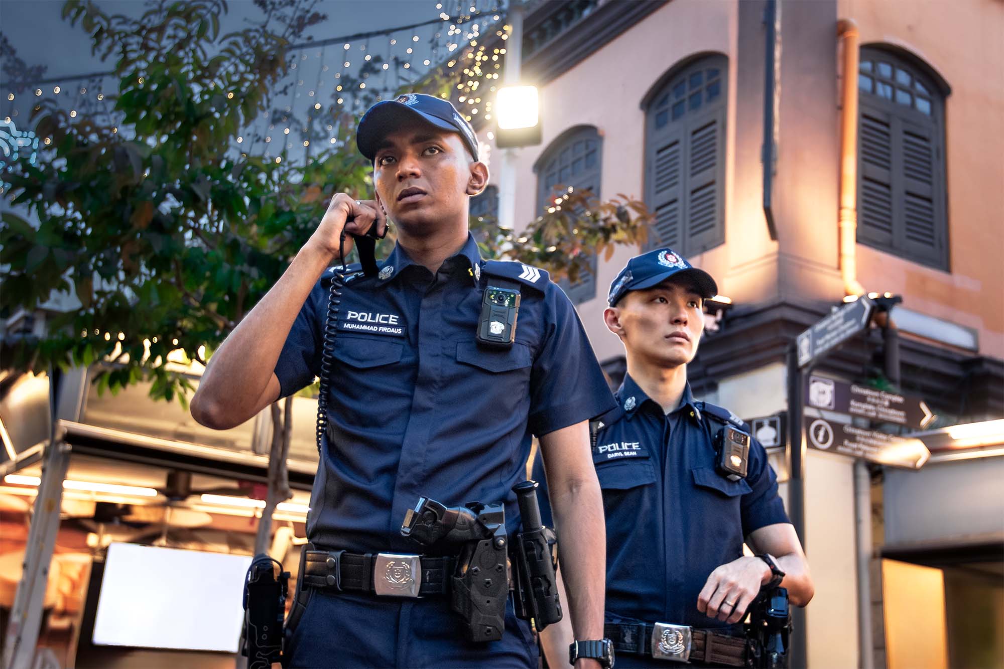 the malay officer is using his palm mic to talk while the other officer is looking out