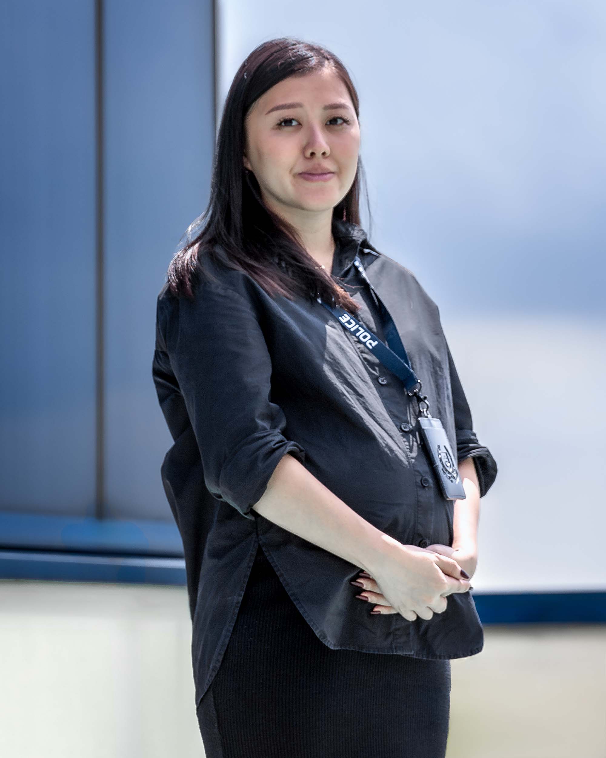 female officer in black gown standing at a rooftop and posing for photo with his arms clasped infront of her