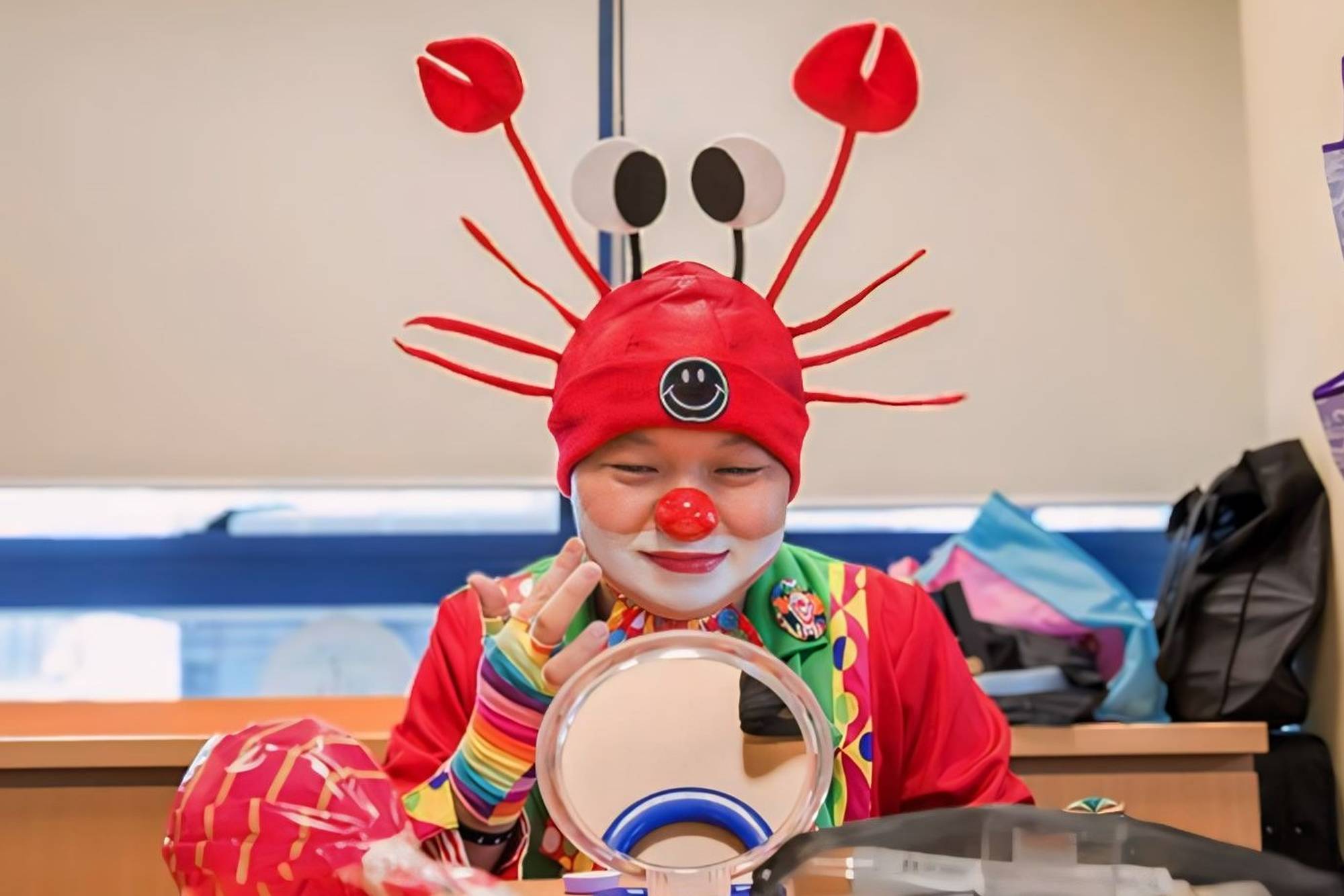 a man dressed as a clown putting on make up and preparing himself, while looking at a handheld mirror