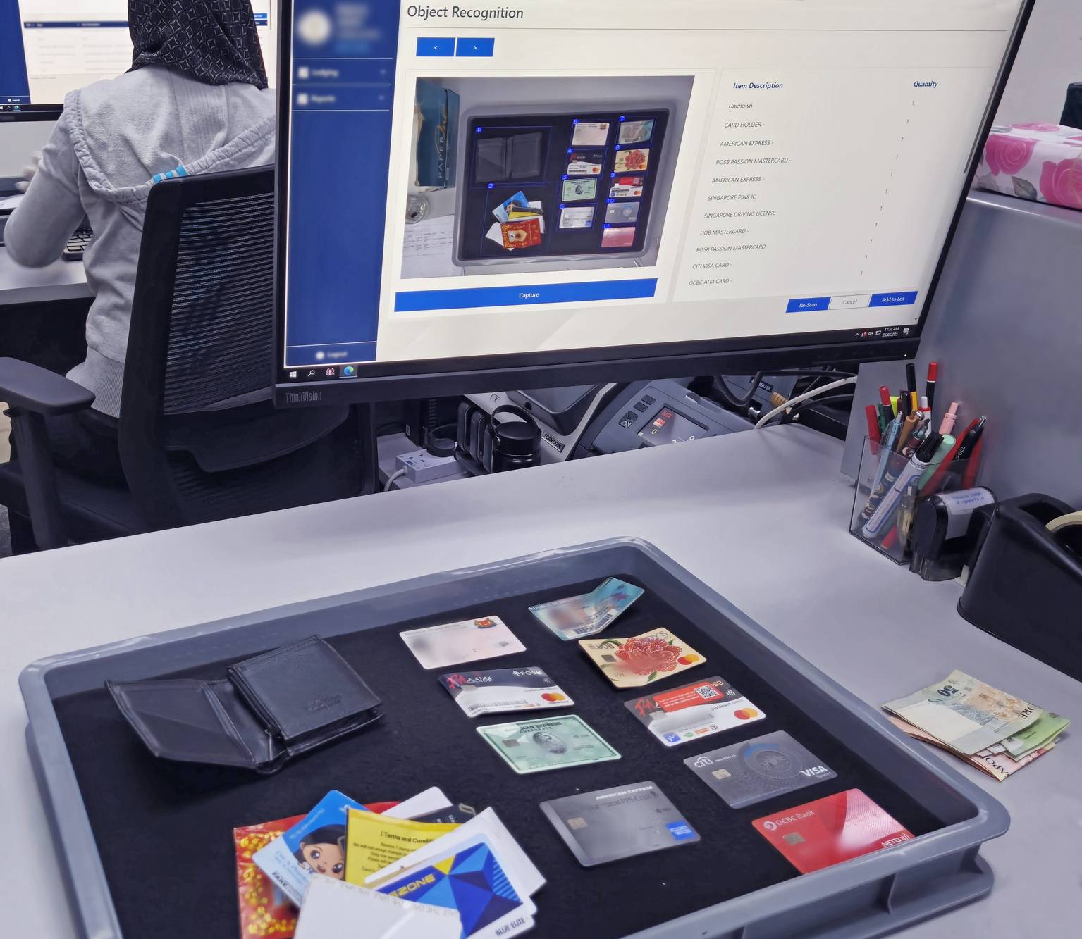 a table with a tray full of someone's belongings that is being captured by a camera, displaying it on the computer screen. The word "object recognition" is seen on the screen