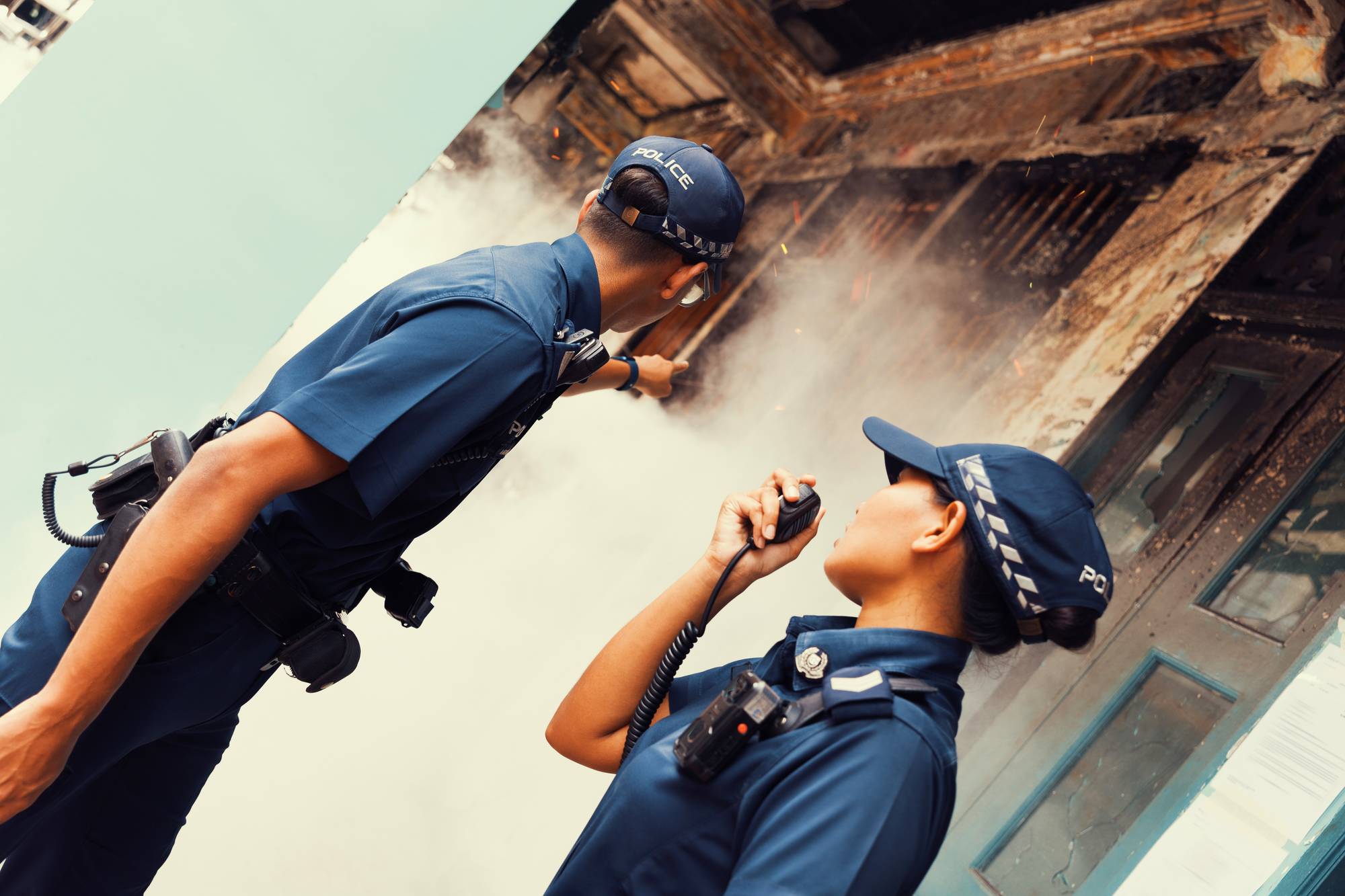 two officers standing outside a burning unit, emitting smoke, while they are on their comms