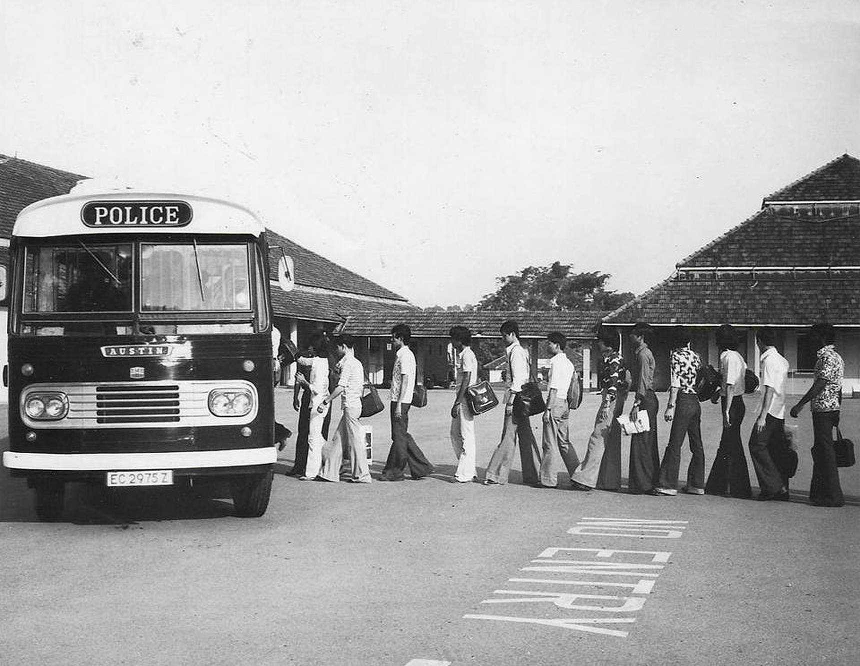 and old police bus is pictured. people are boarding the bus towards the left direction