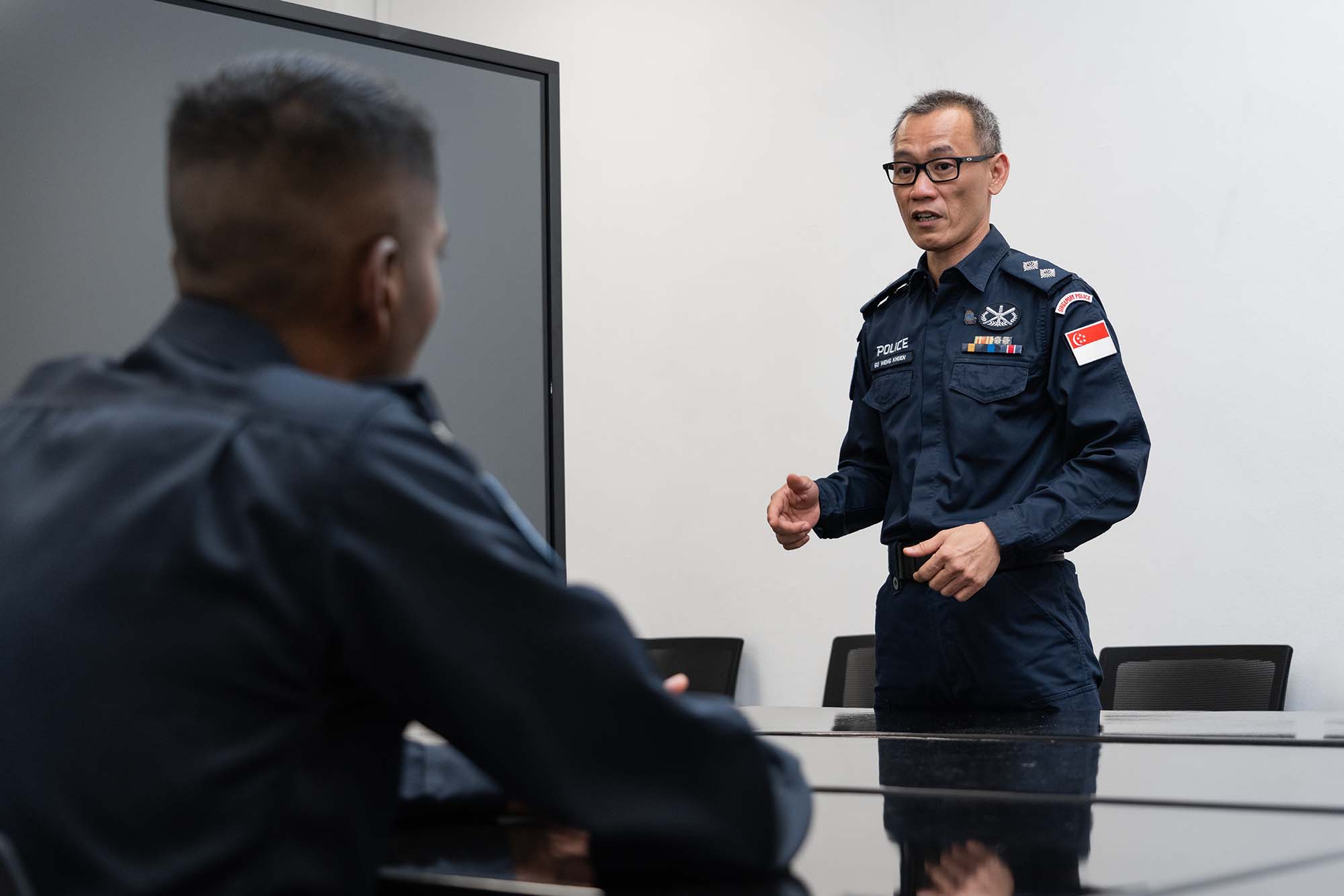 Insp Gu standing up and talking to SI Varan, sharing his experience