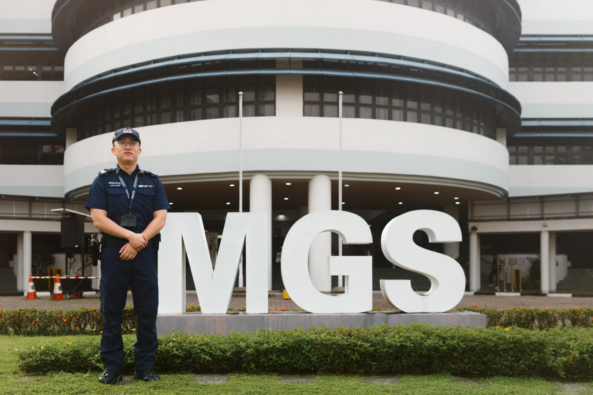 officer in blue police uniform standing infront of a sign that states "MGS"