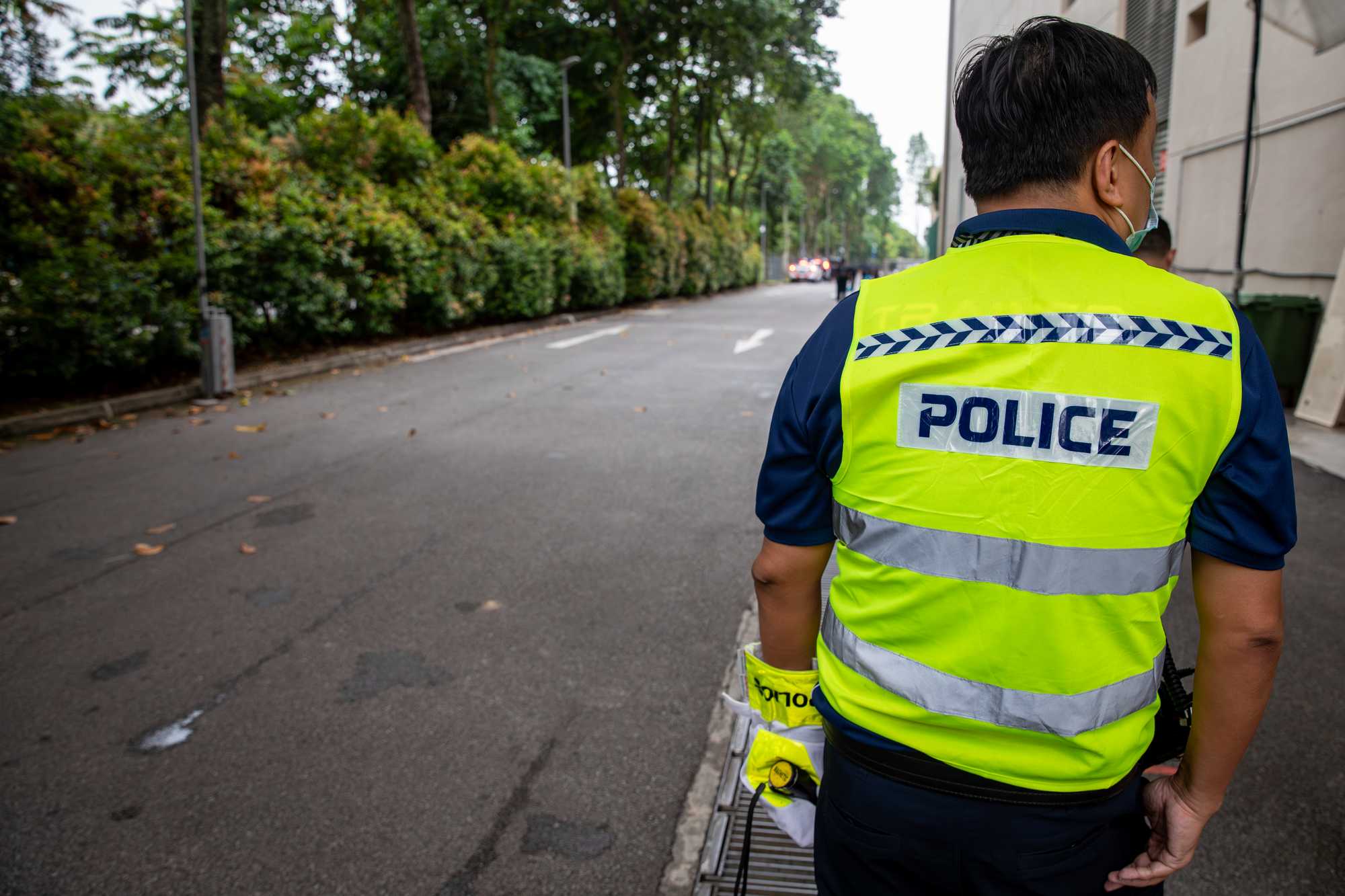 a shot showing the back of an officer who is wearing a brightly coloured luminescent yellow green vest with the word "Police" on it
