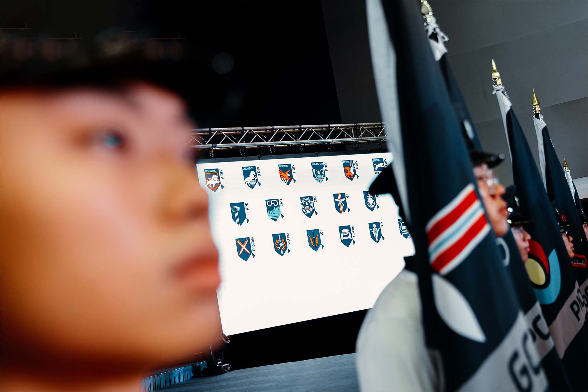 a foreground shot of a blurred face of a flagbearer while the camera focuses on the background of a projector screen, which shows 19 units