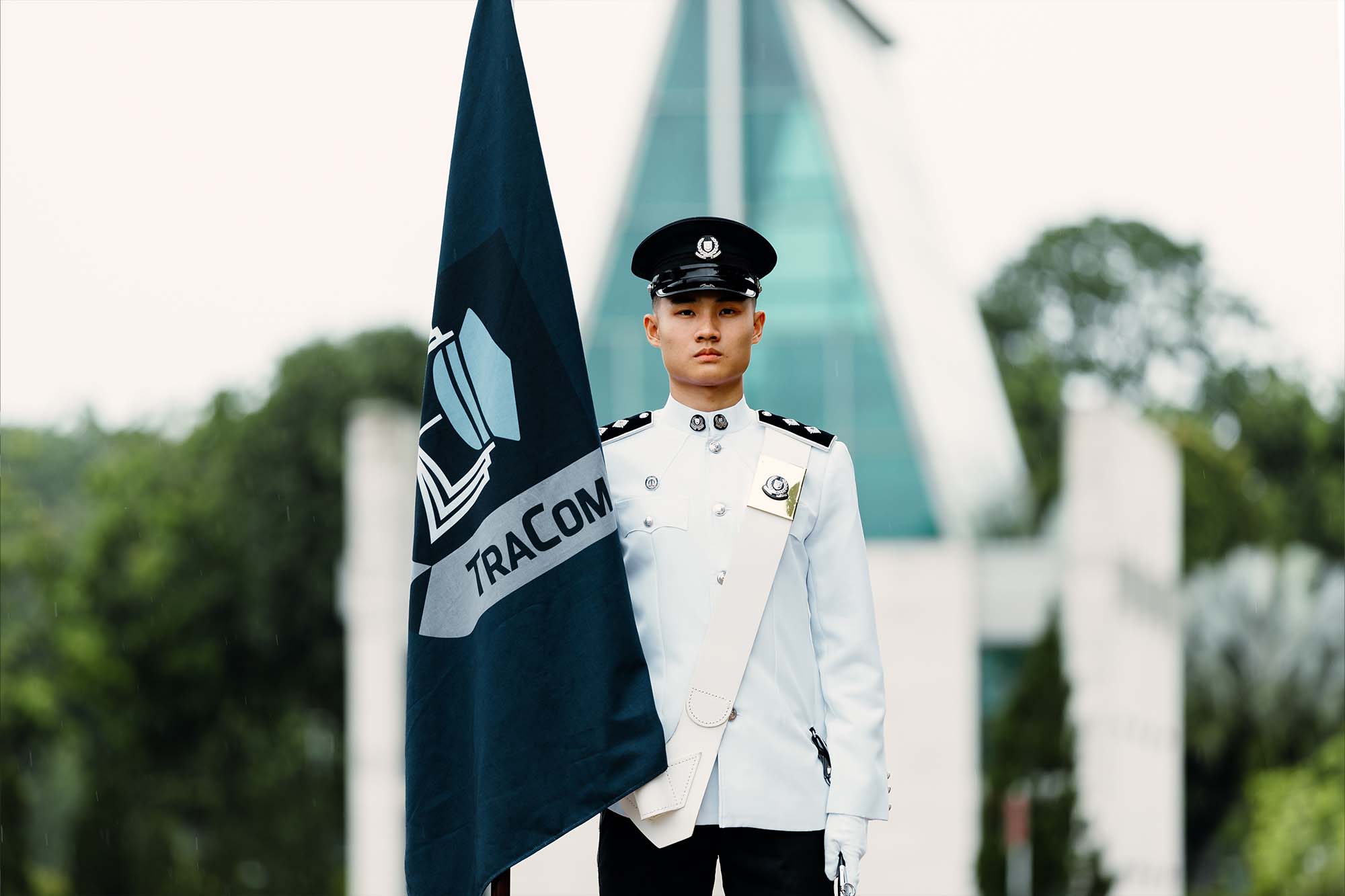 nsi chong standing straight, in white uniform, carrying his flag. He is stout, not smiling and focused