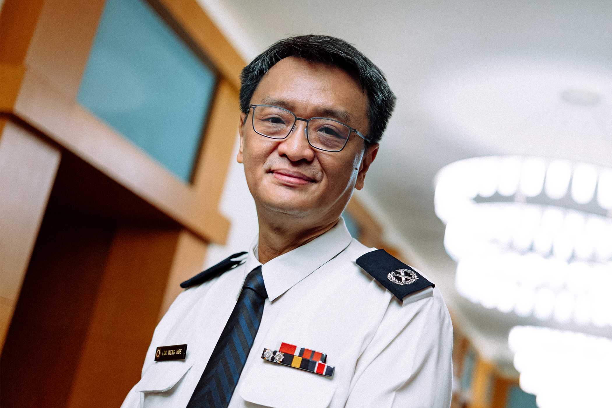 a focused shot of the officer, wearing a ceremonial white uniform and tie, posing. His expression is calm and content