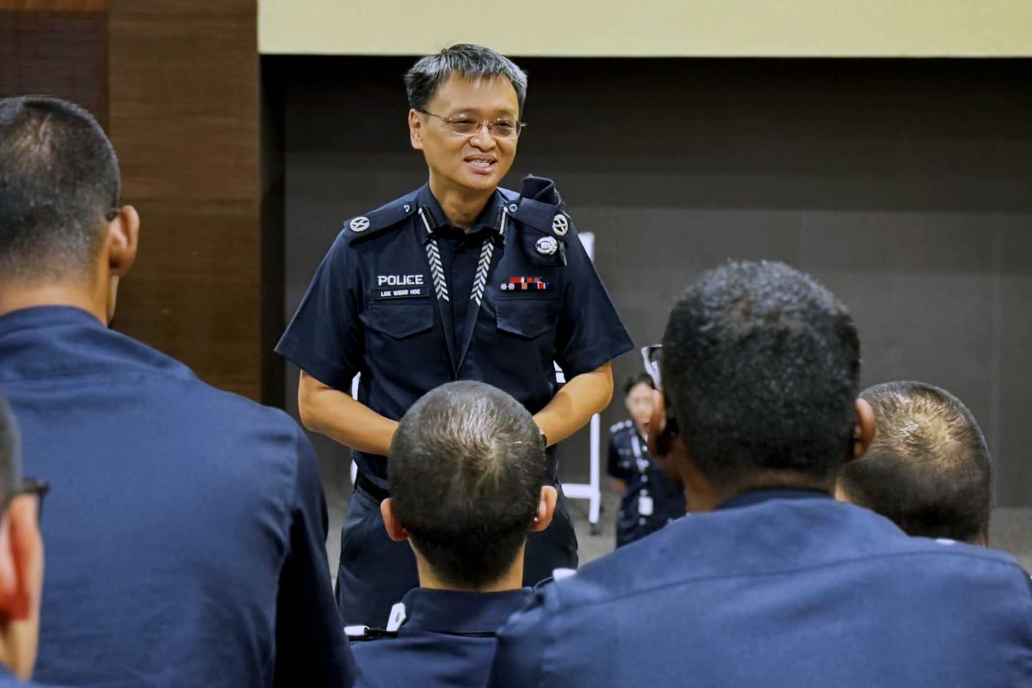 an officer in blue standing in the middle giving a talk to seated officers