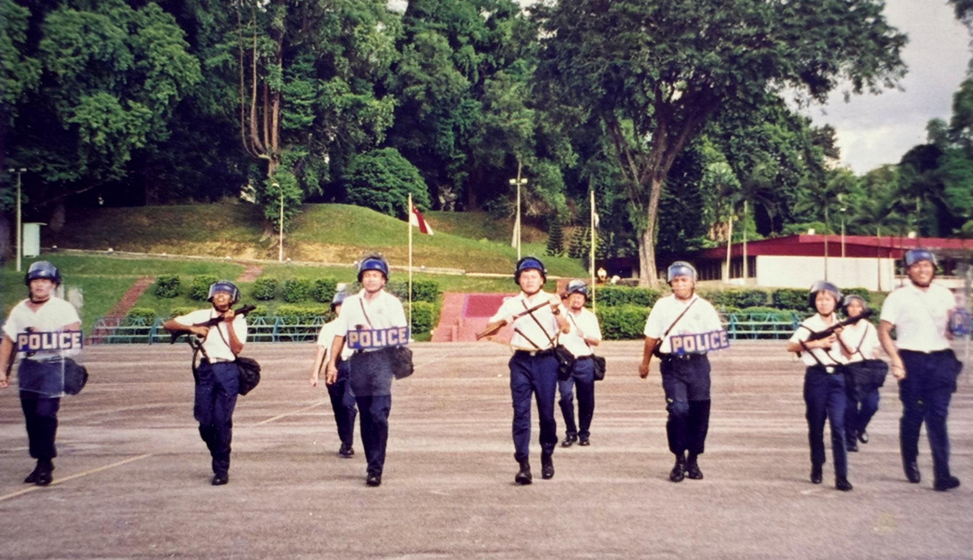 officers in a single horizontal file marching with riot shields