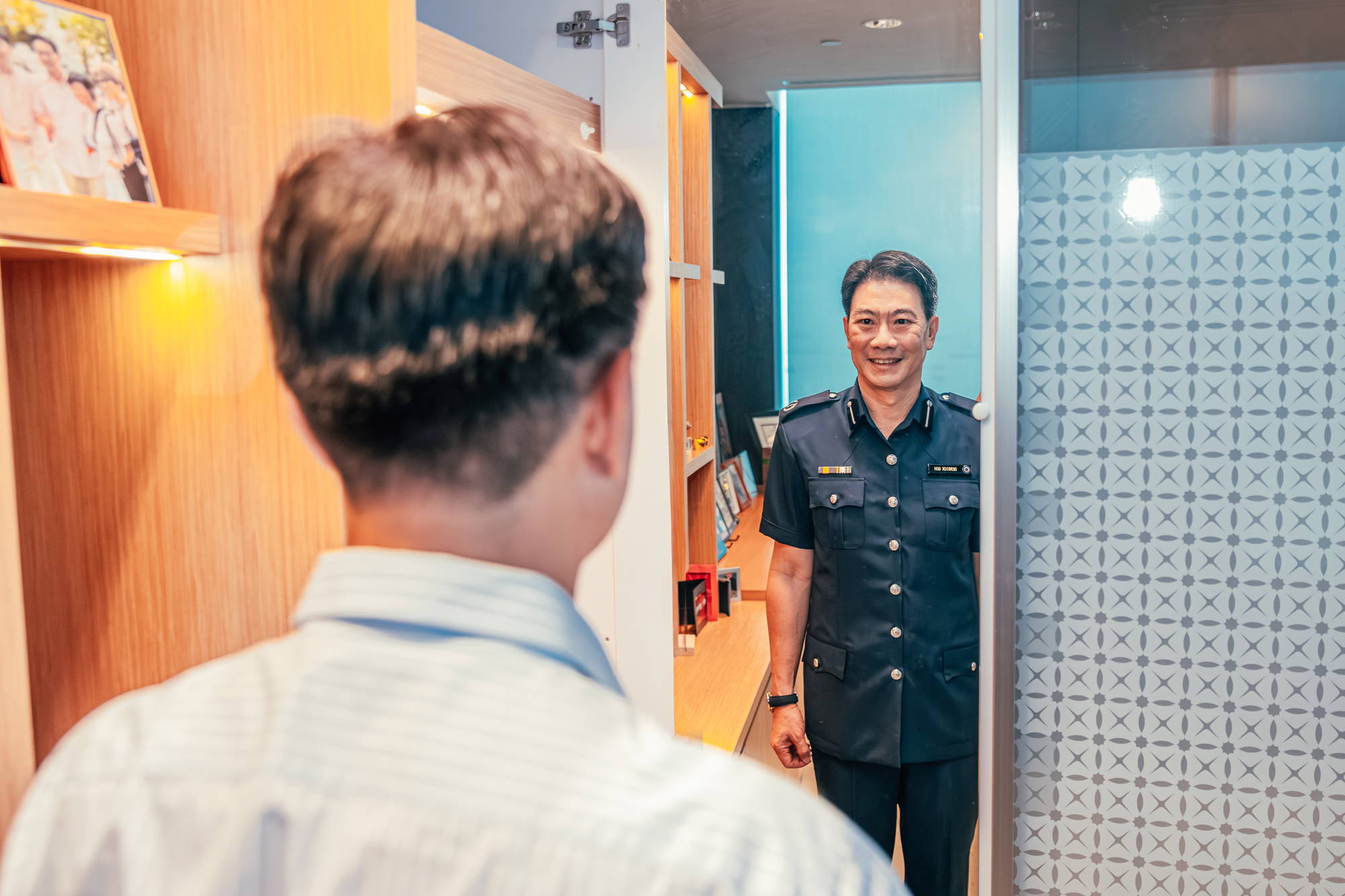 mr derrick goh wearing civvy but standing infront of a mirror which is of him in his police uniform