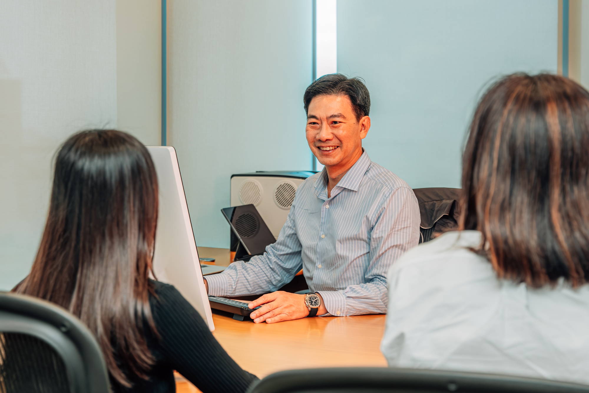 mr derrick goh sitting behind a desk and talking to two colleagues