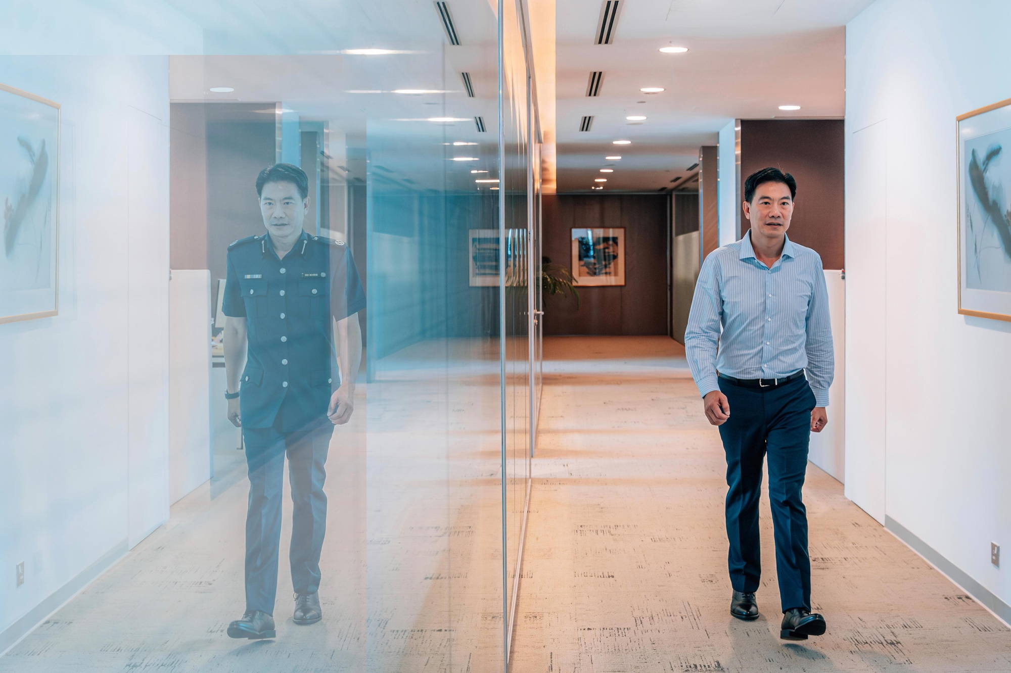 he is walking towards the camera along his office corridor but the reflection on the glass panel shows him in uniform