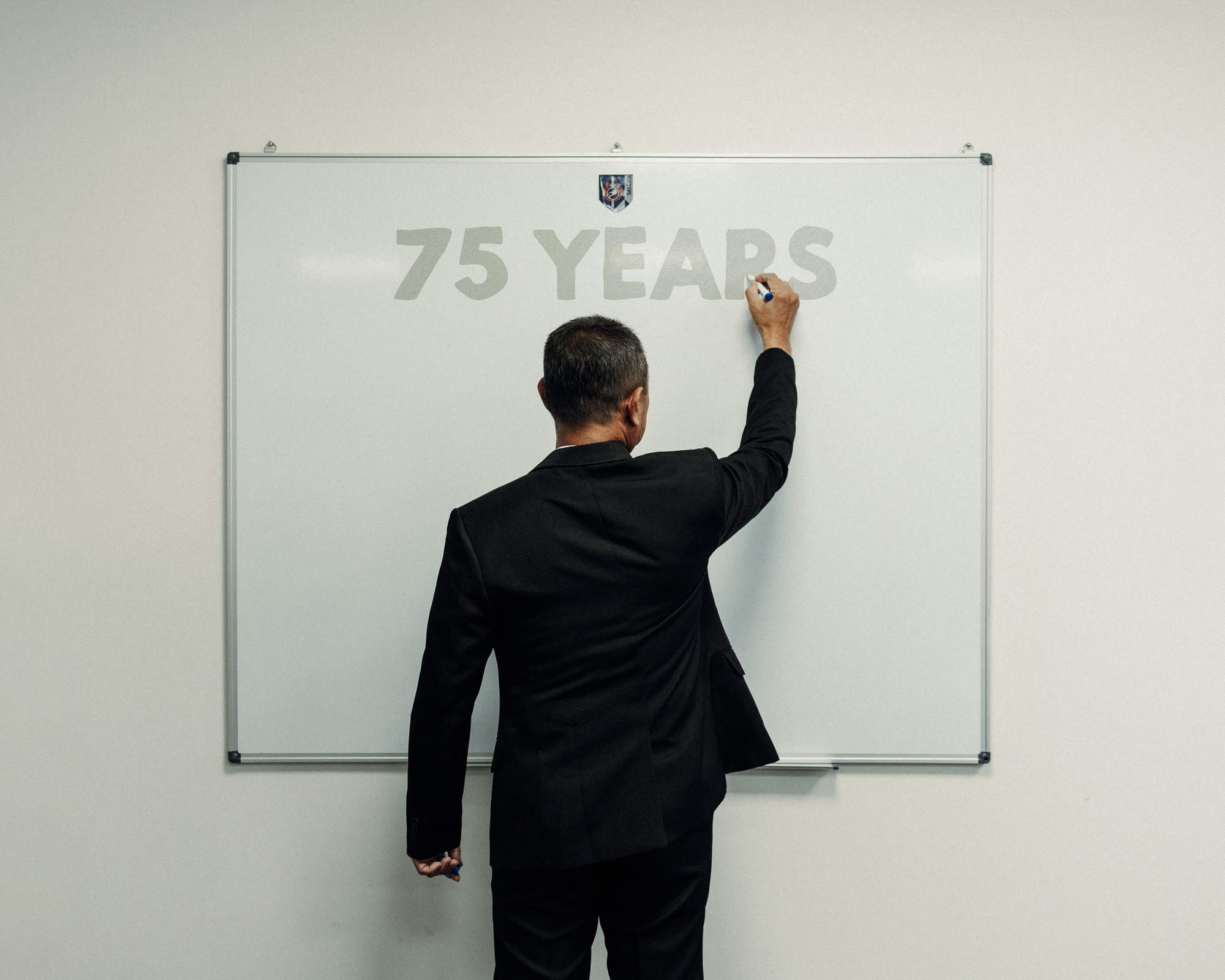 an officer in suit and tie standing infront of a white board writing the numeric 75 on the board