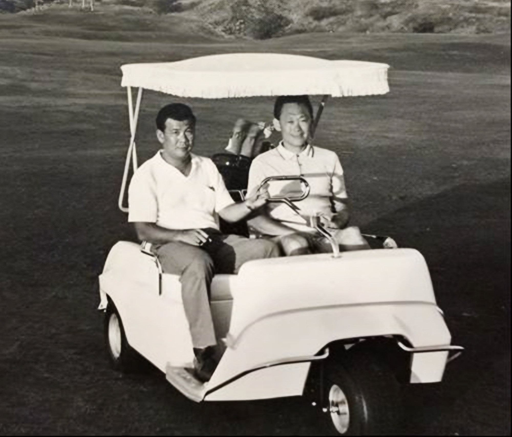 ac tan in a buggy with mm lee, both wearing a light top. The photo is monochromed.