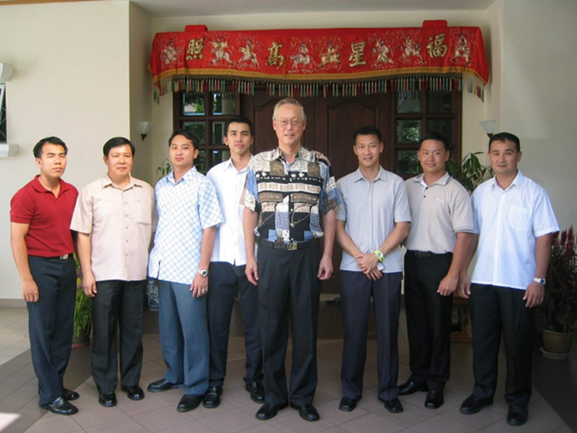 officers in civilian attire and part of a security detail standing infront of a house door entrance with chinese new decoration, while ESM goh is standing in the middle