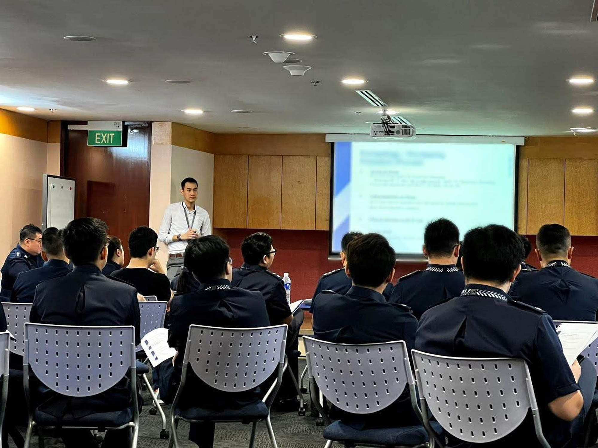 jason wearing small casual and briefing a room of officers wearing police uniform