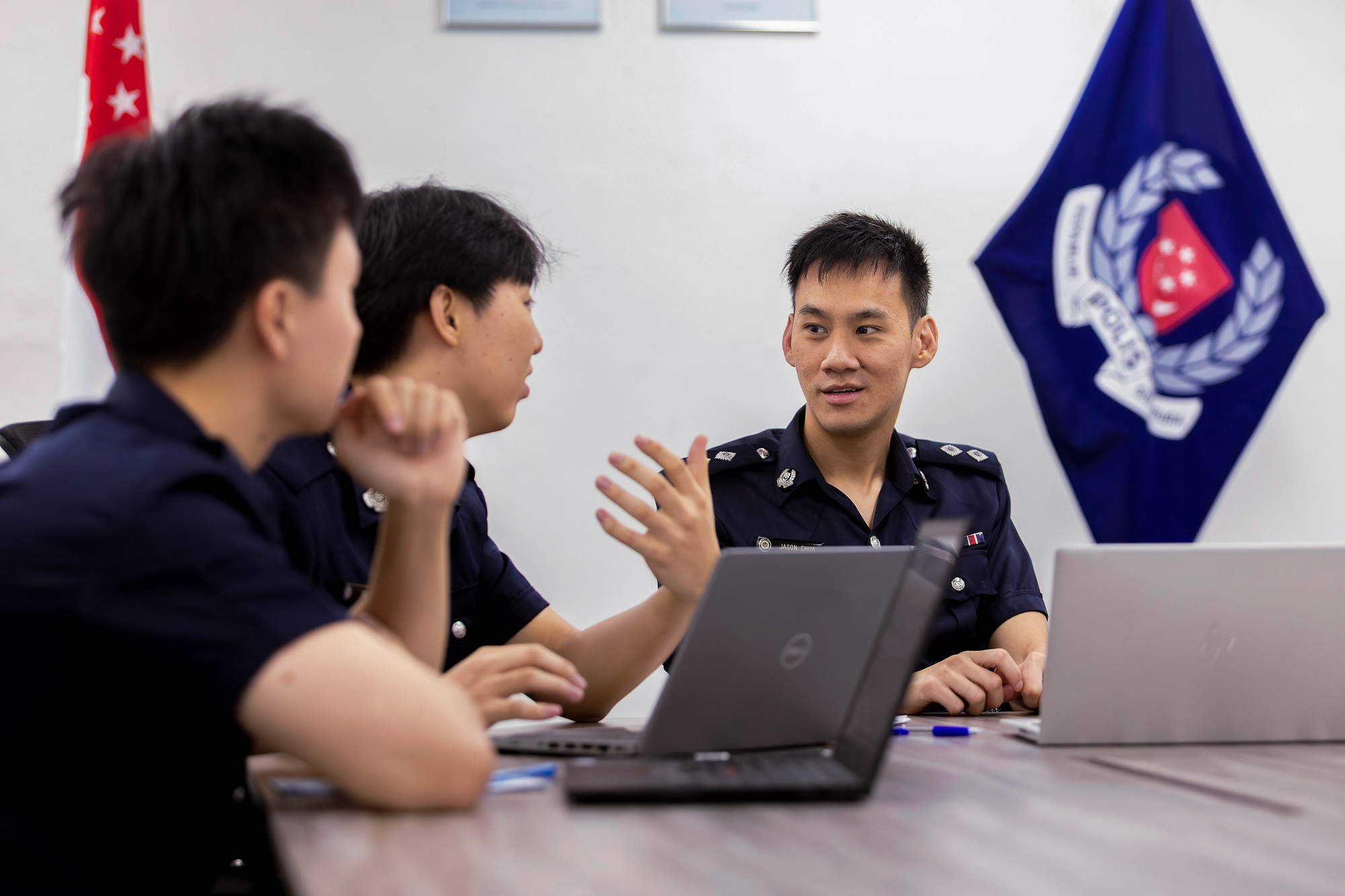 jason and two PNSFs in a meeting room sitting by a white table. Behind them is the SPF flag