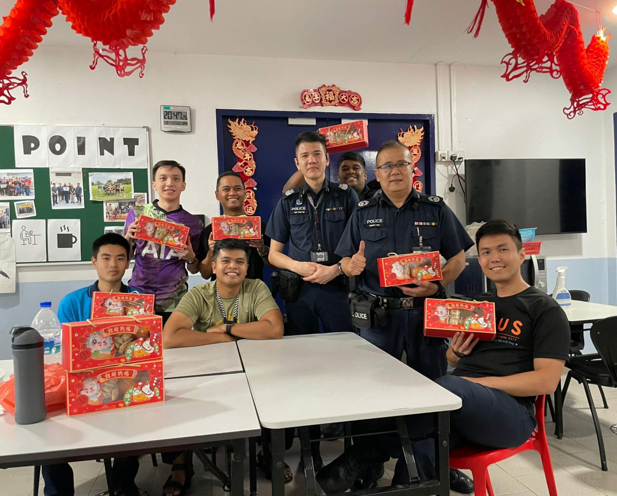 a team photo of him and his officers seated at a pantry setting, with CNY decorations trung from the ceiling. Some officers are holding CNY goodies.