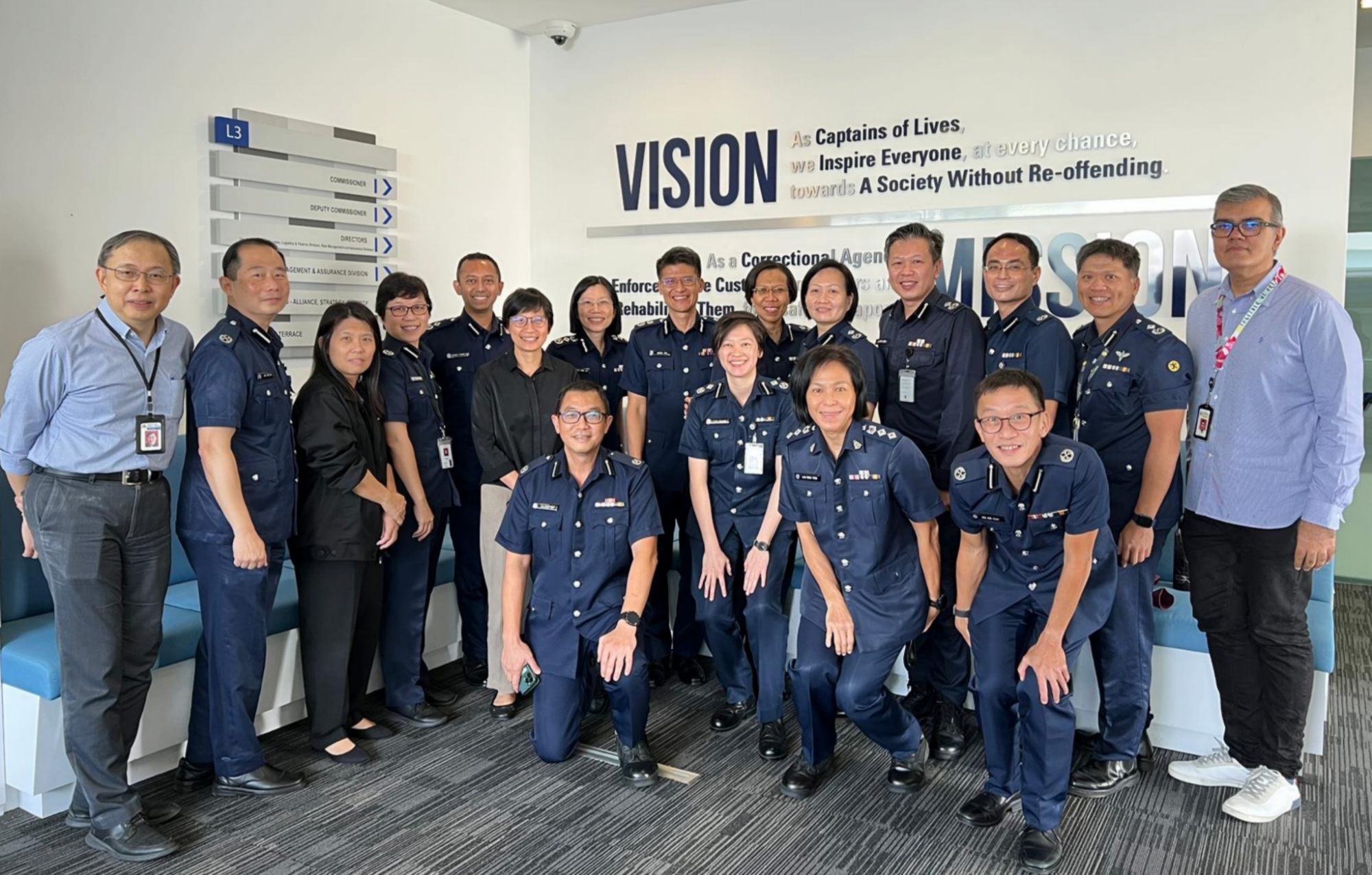 A group photo taken in an office setting with a large group of officers posing 